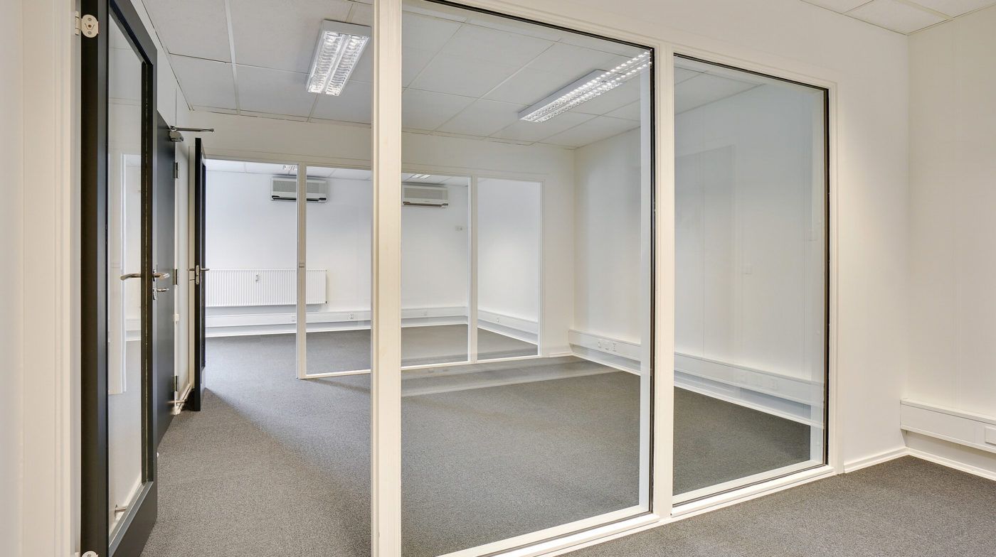 En tom kontorrum med lyse, hvide vægge og glasdøre og -ruder, tæt på jernbanegade 75-77 i Middelfart