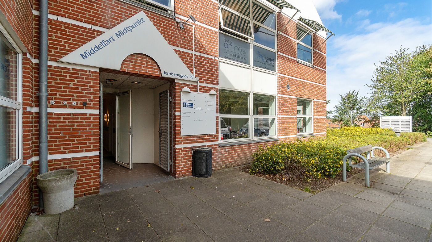 Middelfart Midtpunkt er en slank bygning med høj gulv til loft højde og flere vinduer i centrum af Middelfart. En hvid skilt