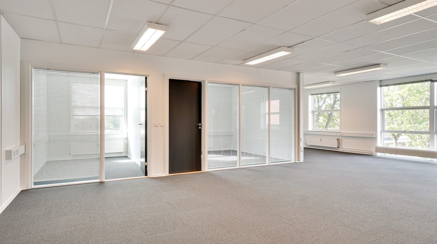 Tomt kontor med glasdøre, hvide vægge, højt til loftet, lysekroner og vinduer med jalousier