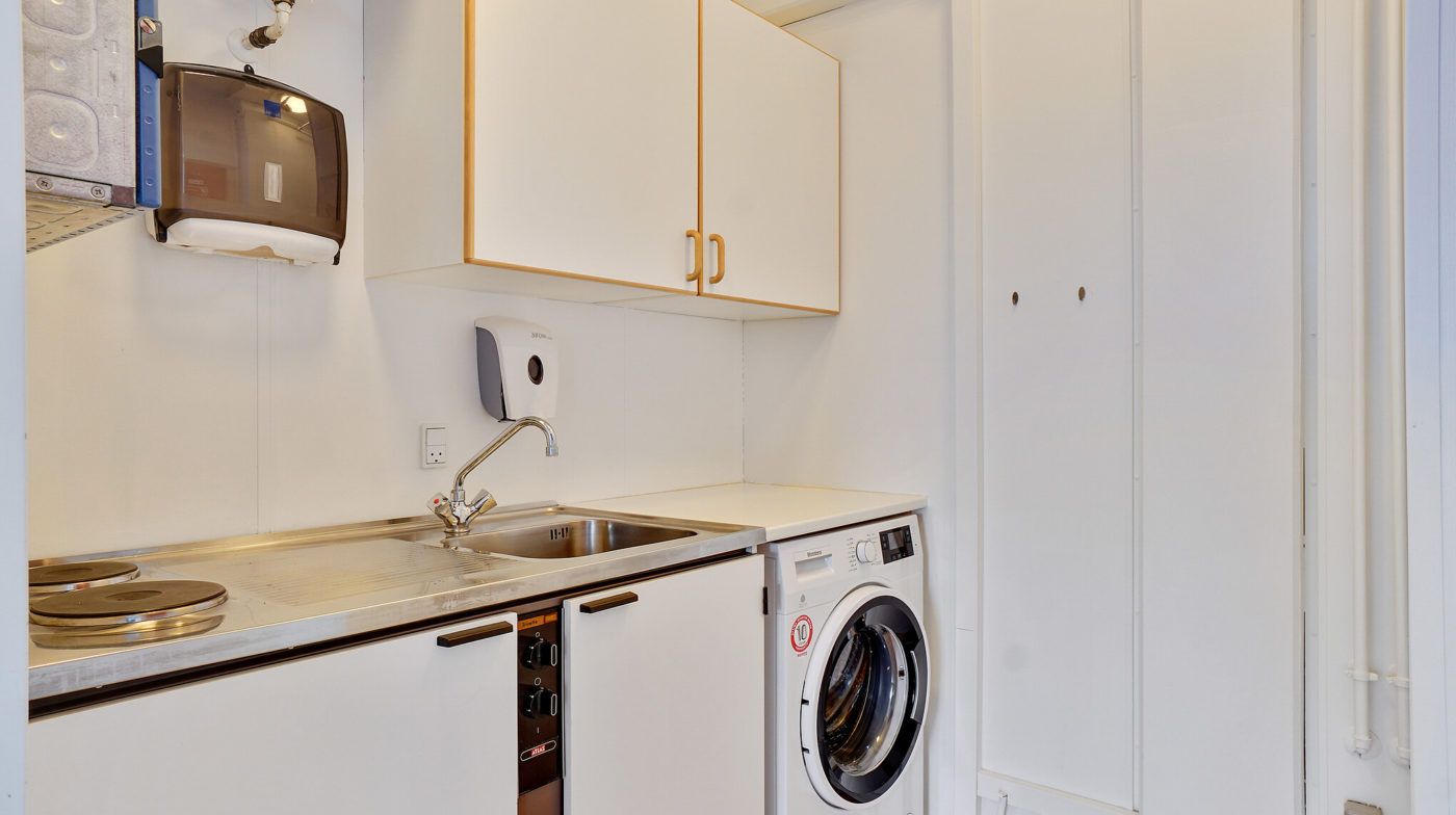Et lille tekøkken med ovn, vaskemaskine, håndklædeautomat og enkelt personvask