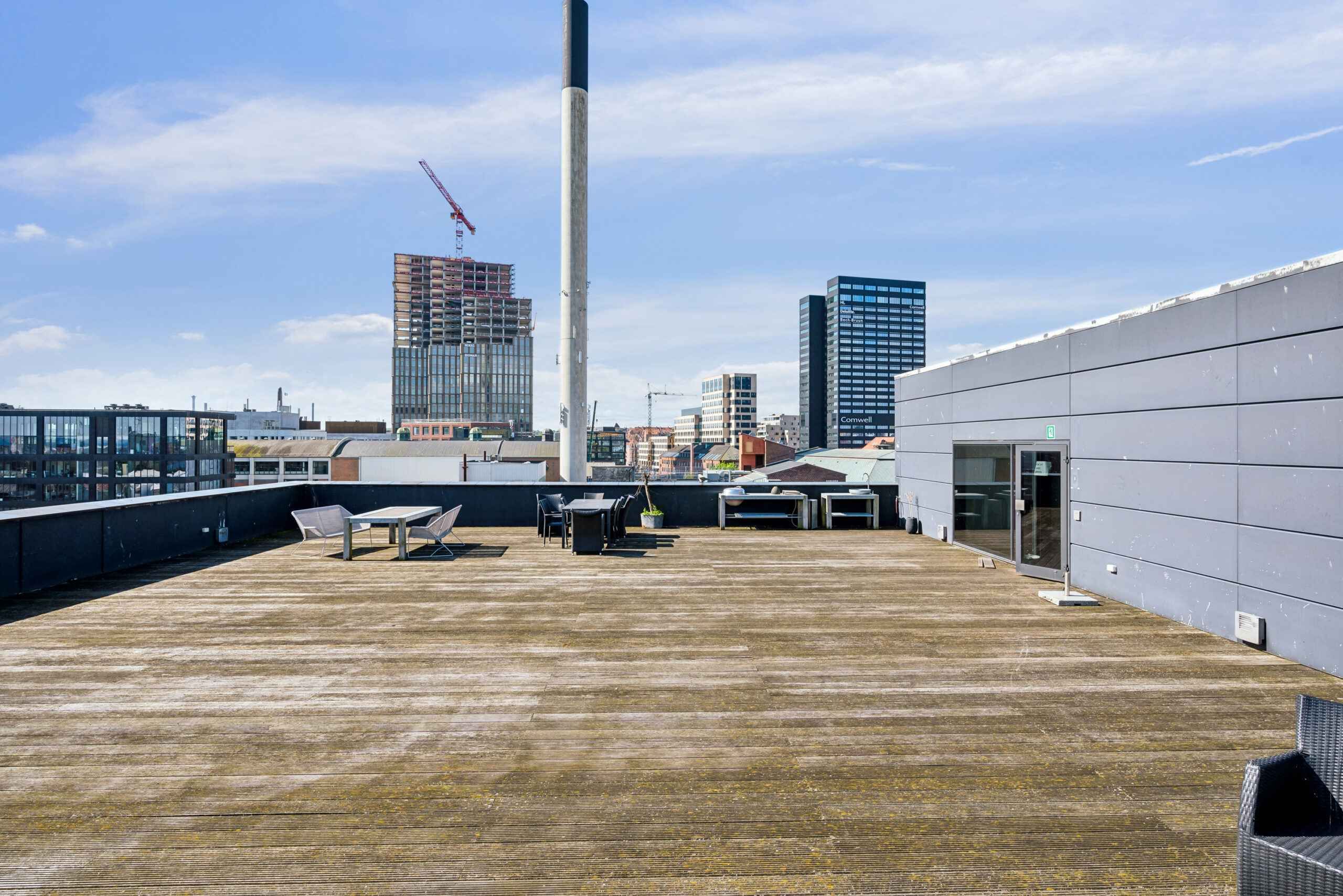 Moderne kontor med udsigt over Aarhus bymidte, terrasse med møbler, og i baggrunden bygninger og et tårn under opførelse