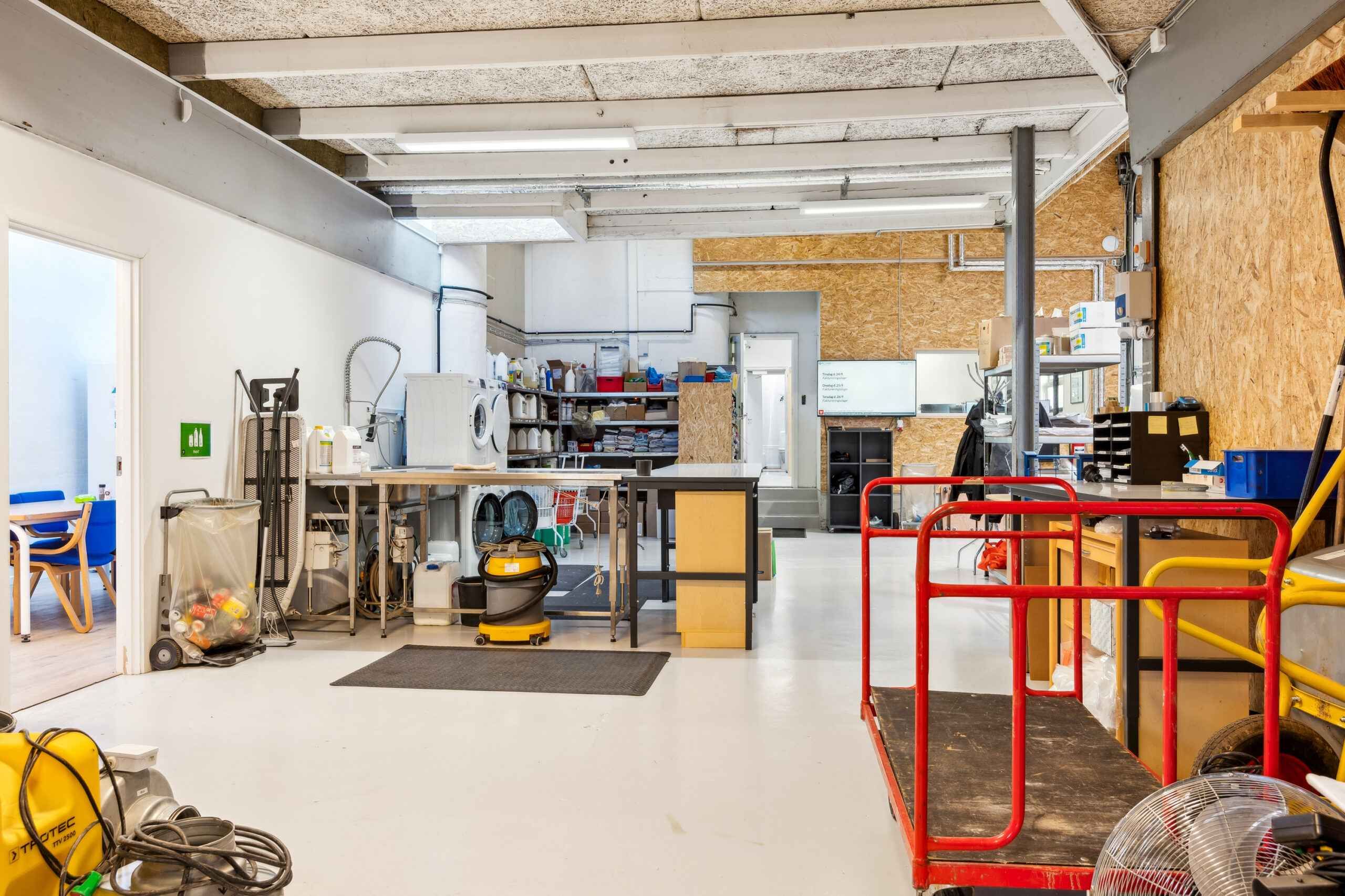 Remmeborde, højre side af et rum med gulve, vægge, møbler og redskaber. Trækvogn og vaskemaskine med flere kasser.