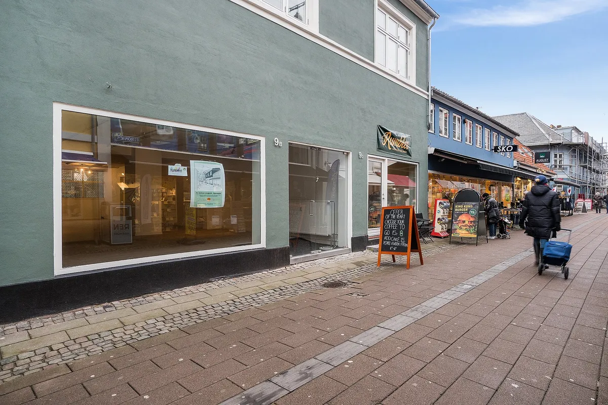 En bred gågade med tomme butikker og gående folk, samt en udrullet vogne og skilte med reklamer og tekst