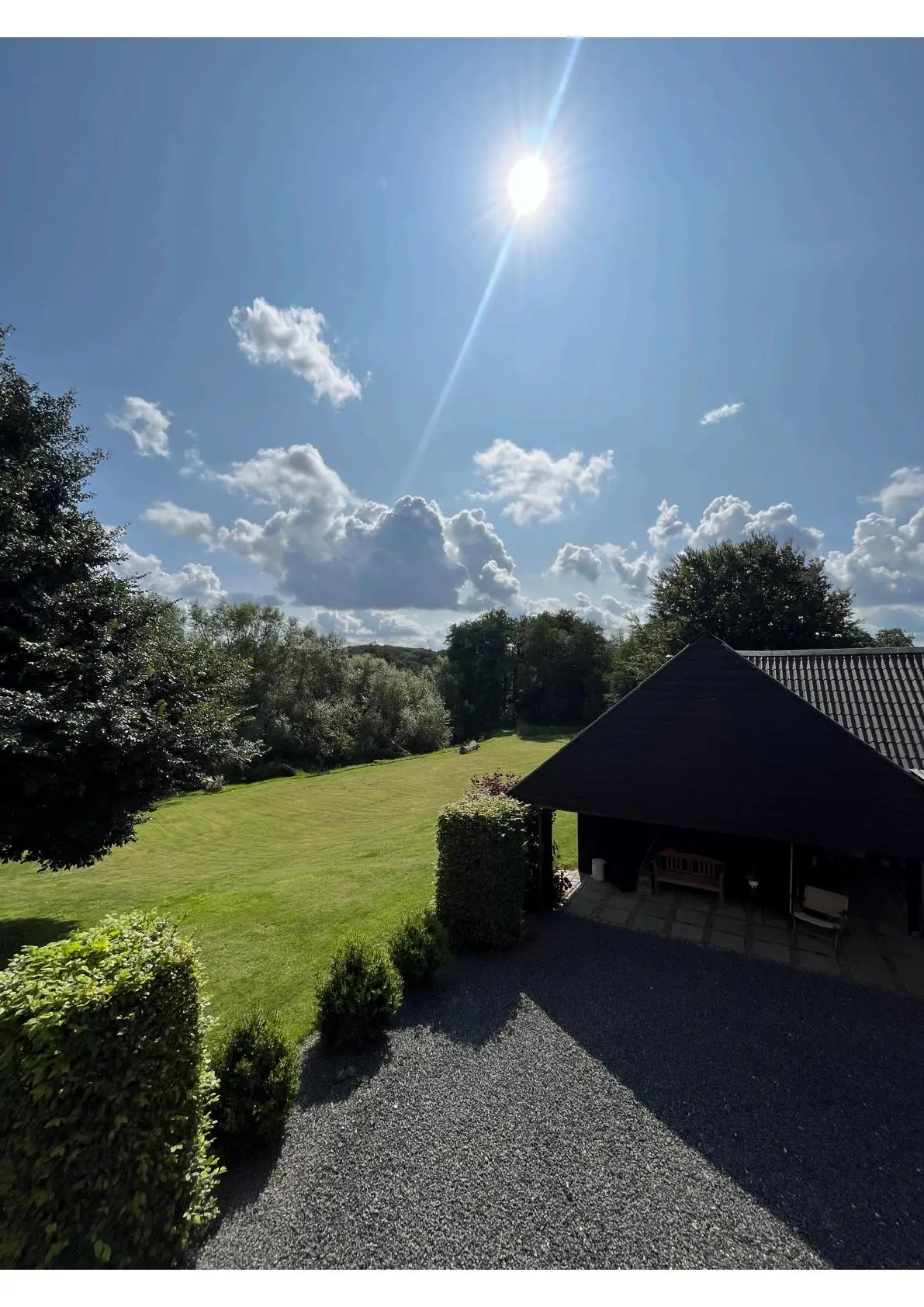 En grøn græsplæne med en solskinende himmel og en skur til parkering af biler med en træbænk i udkanten af skur