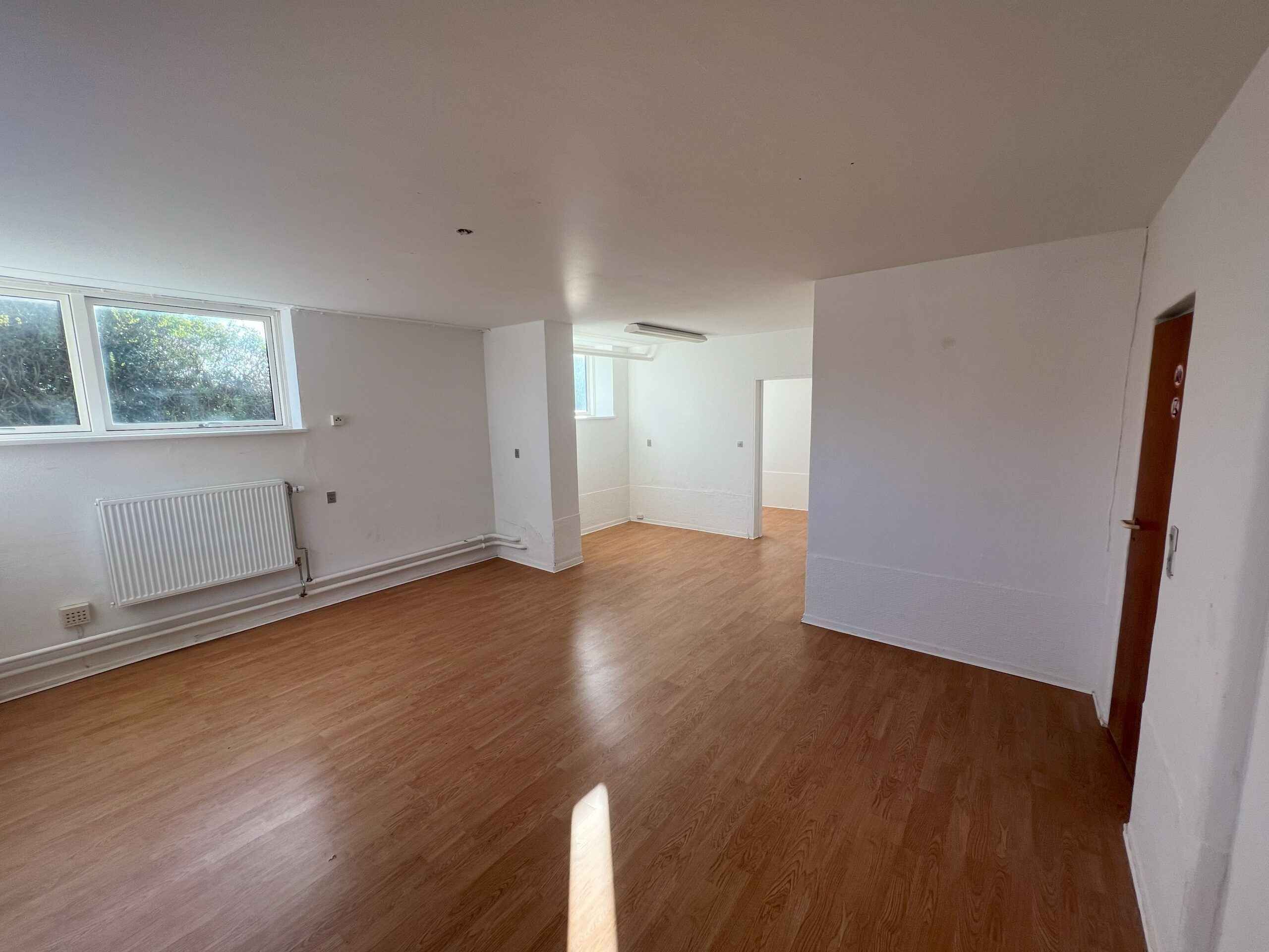 Rummeligt og lyst erhvervslokale med trægulv, hvide vægge og et vindue, der stiger ud i gården