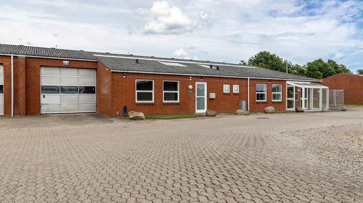 Nyborg Erhvervspark med stor synlig facade fra Fynsvej. Moderne røde bygning med solpaneler, garage og glasdøre. Store sten