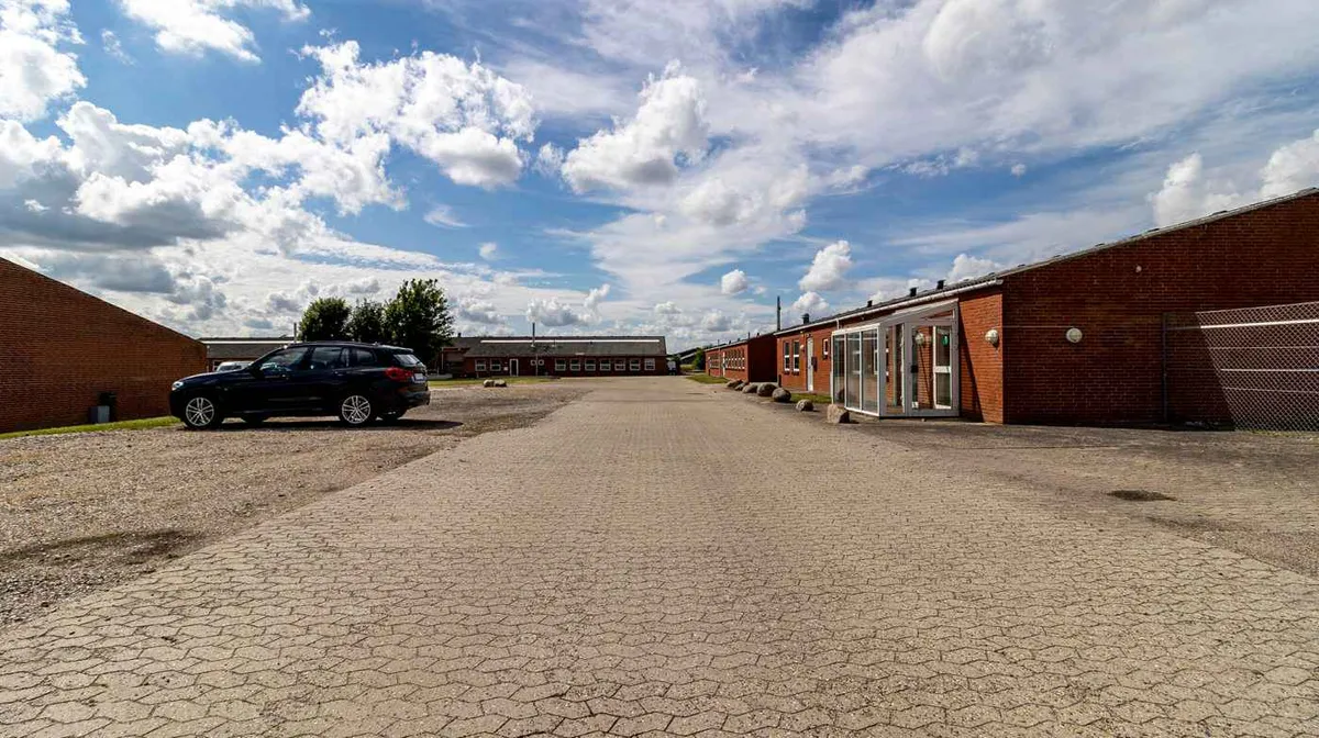 En længe, bred asfaltvej mellem røde bygninger med store glasruder og store høje buede tag