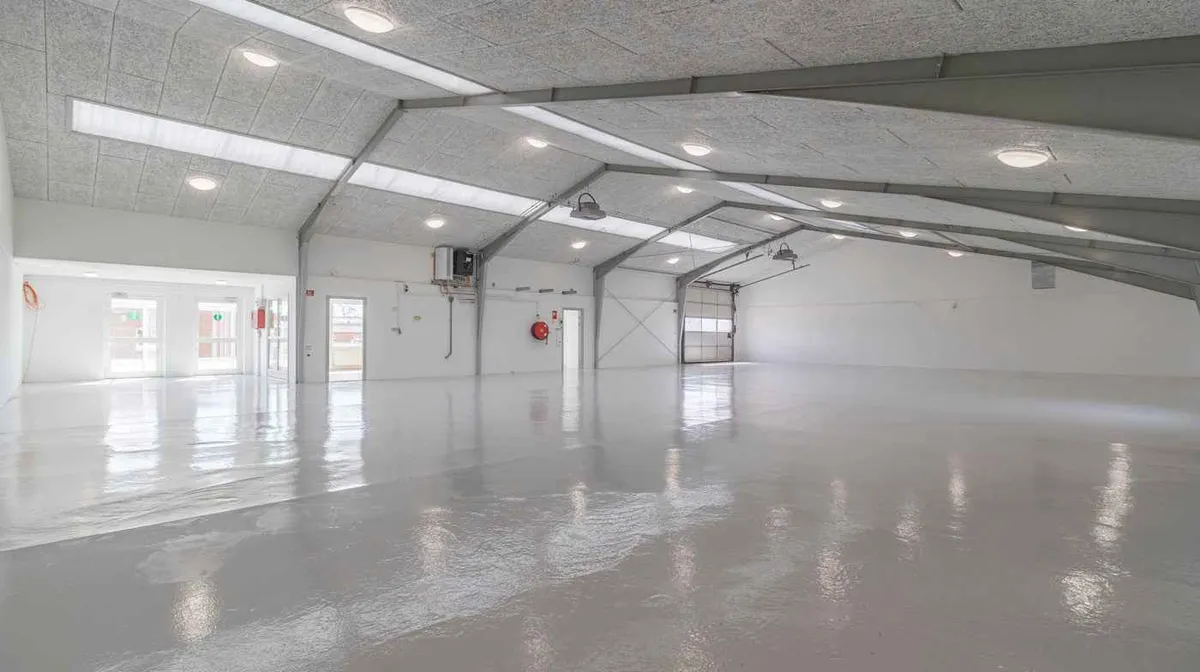 Rummelig lagerhal med hvide vægge, gulv og loft samt moderne belysning. Lejligheden er perfekt til lageropbevaring.