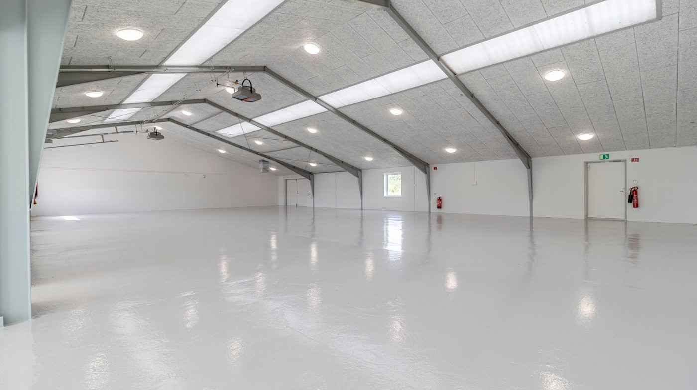 Et stort, rummeligt og renset værksted med hvide vægge og loft, moderne gulvbelægning, flere lysekroner og to brandhætter
