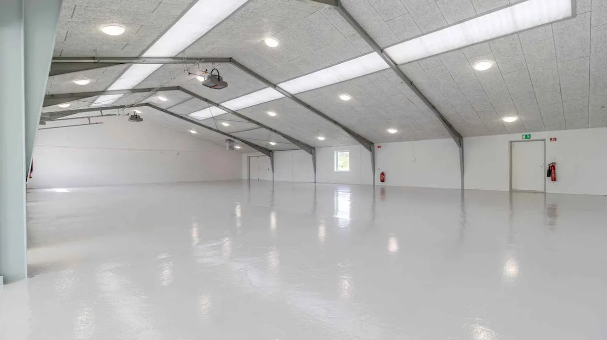 Et stort, rummeligt og renset værksted med hvide vægge og loft, moderne gulvbelægning, flere lysekroner og to brandhætter