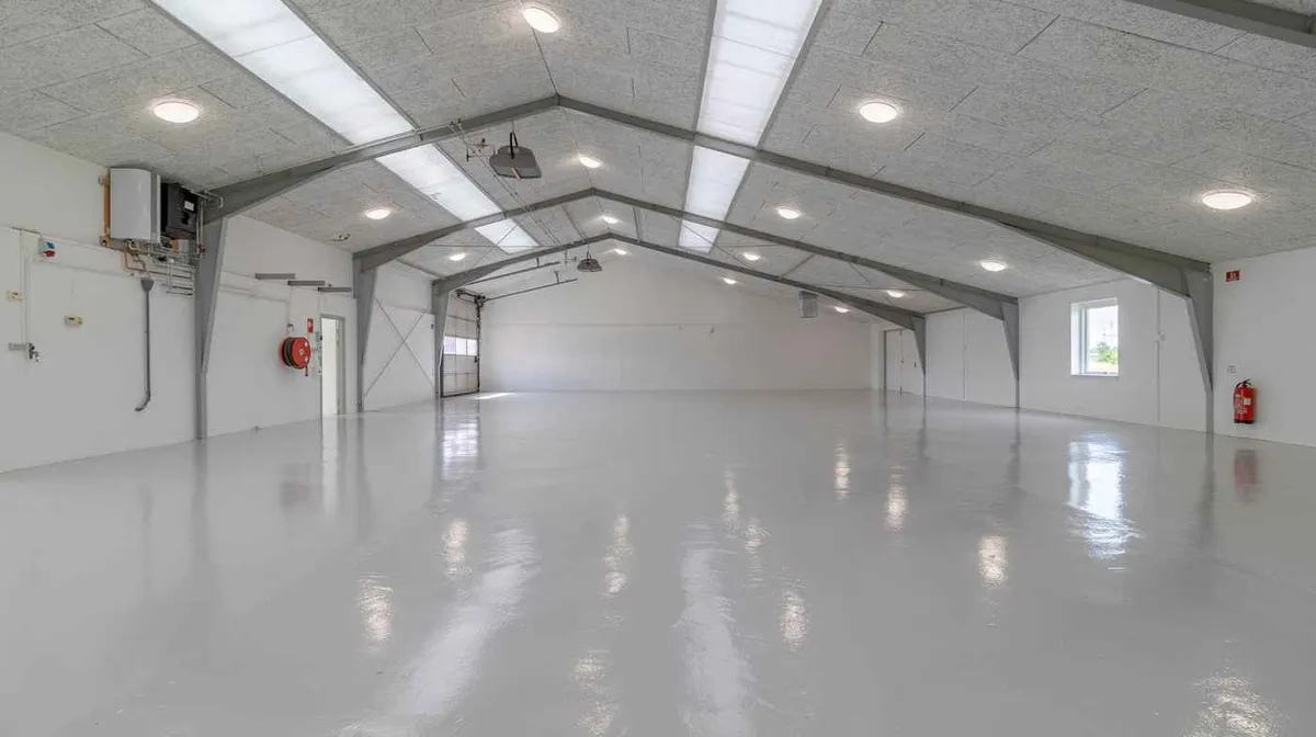 Lang, stor, hvid, ren og ny fabrikshal med højloft og lysekroner, der reflekterer lys på gulvet