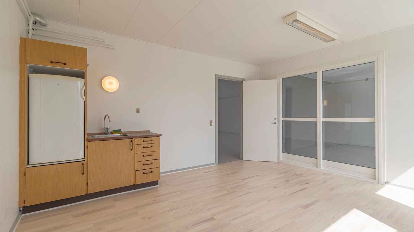 Lejlighed med moderne køkken og en stor køleskab samt en åben dør, der giver udsigt til et glasparti og udendørsområdet