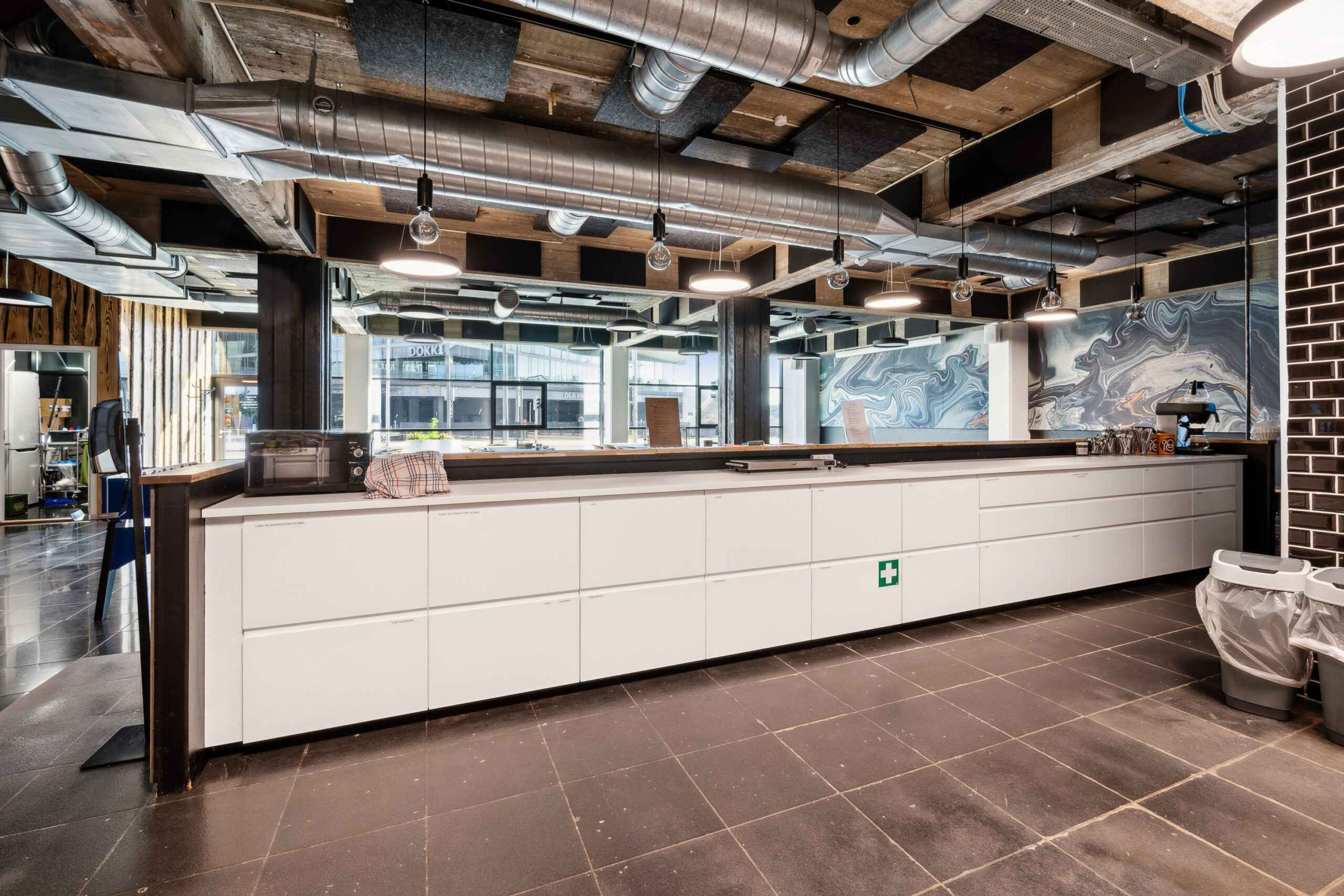 Regleret lokale med højt loft, moderne udstyret køkken med hvide skuffer og en stor arbejdsflade, samt tøjstativ og