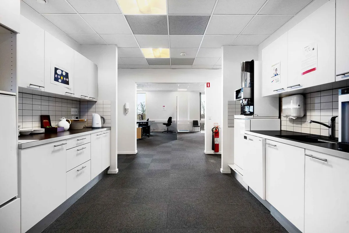Moderne kontor med hvide vægge og møbler, gulv med mørk gulvbelægning, en skrivebordsstol og rødt brandslukker.
