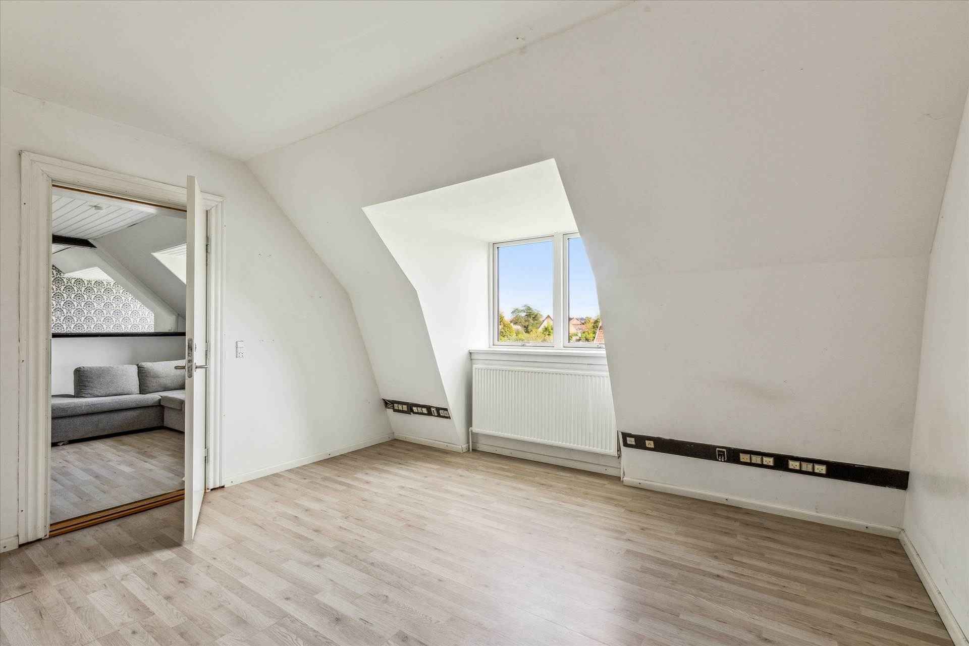 Et moderne, tomt værelse med lysegul vinylgulv og hvide vægge samt et skråt vindue, der giver masser af naturligt lys og