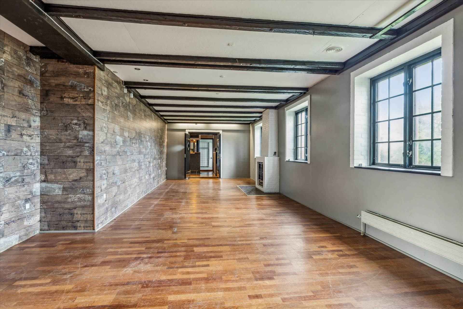 Lejlighed med stor hall og lyse trægulve. En skorsten og to store vinduer med udsigt til gaden.