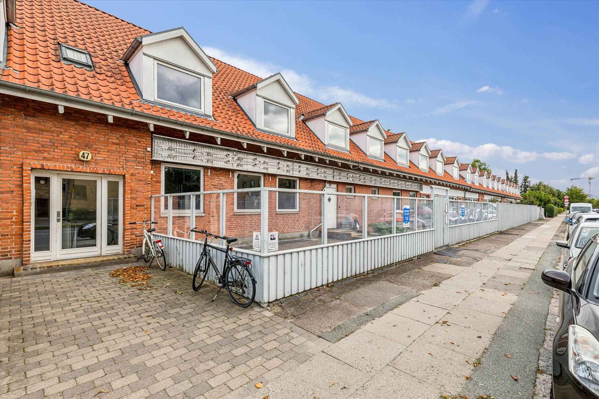 En rød murstensbygning med nummer 47 og parkerede biler på siden af gaden med to cykler parkeret foran