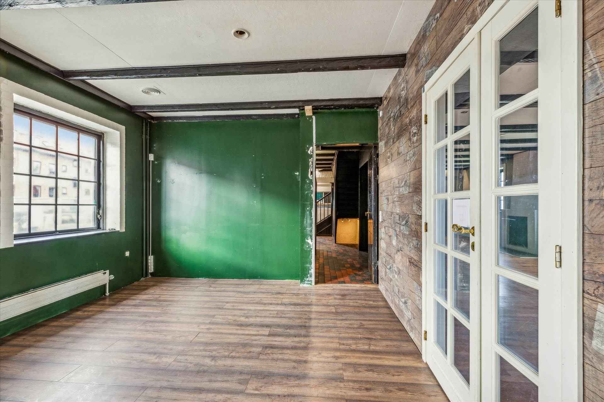 En tom erhvervslejlighed med lysegrå gulvfliser, grønne vægge og hvide ruder samt en hvid dør og udgang til en trappeopgang