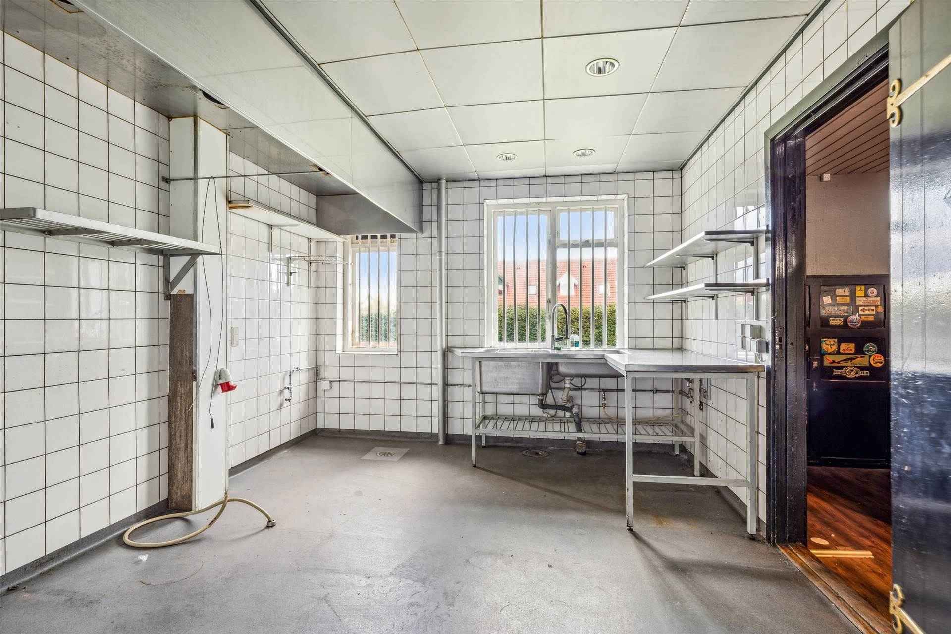 Et rum med hvide kakler, et vindue med ruder, et køkken med vask, et skab og en åben dør, der fører til et andet rum