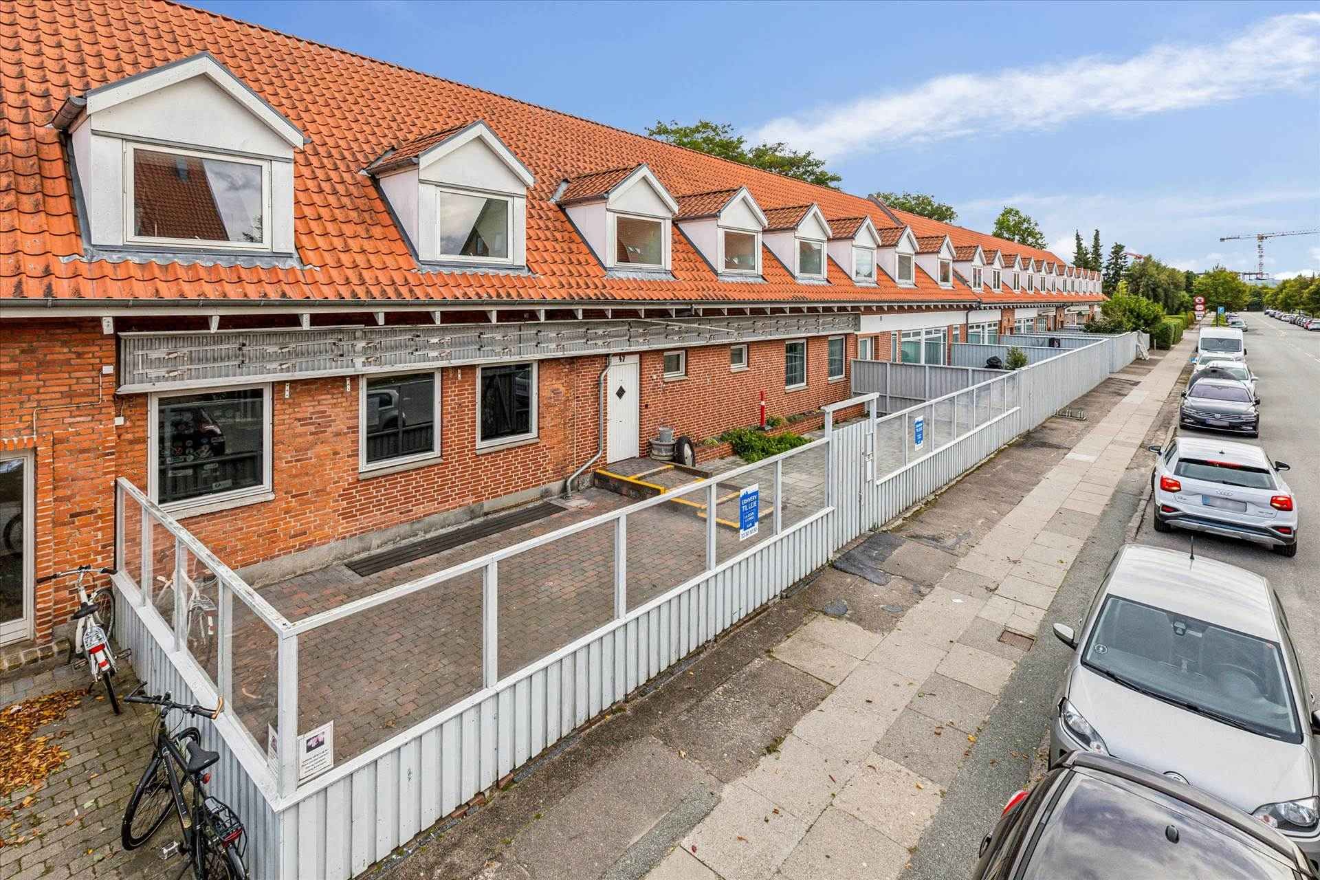 Flere lejligheder med parkering og cykelstel langs en bred gadekante med en række parkerede biler