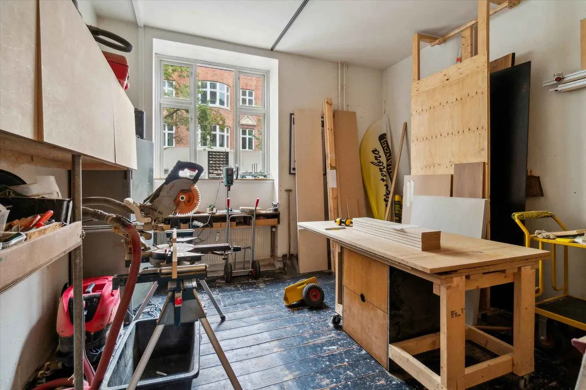 En stor værkstedsrum med træbord, slibemaskine, værktøjsreol og mange værktøj.