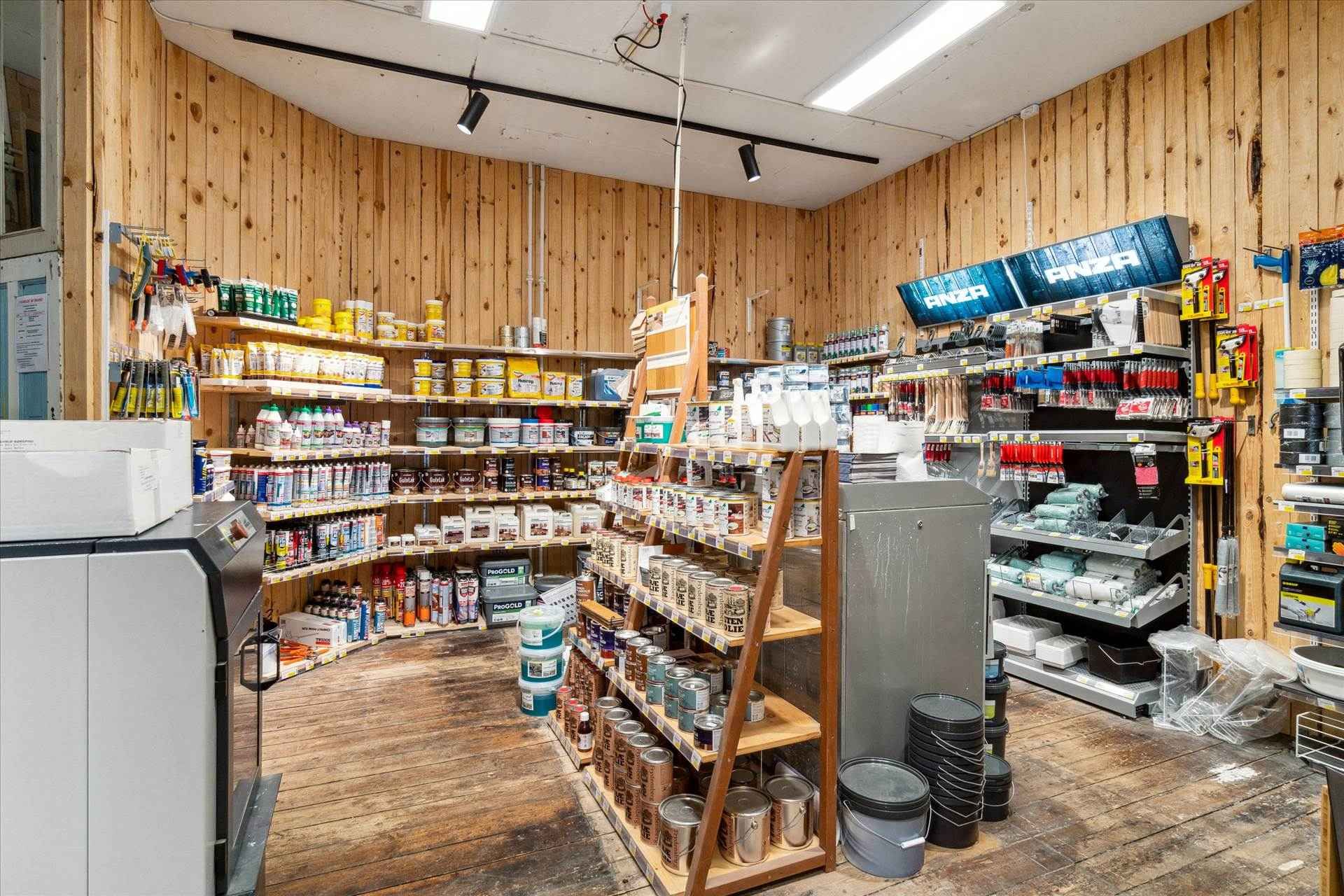 En stor butik med trævægge og højt til loftet. Der er lagerreoler med diverse maling, bøsser og værktøj. Der er en stor