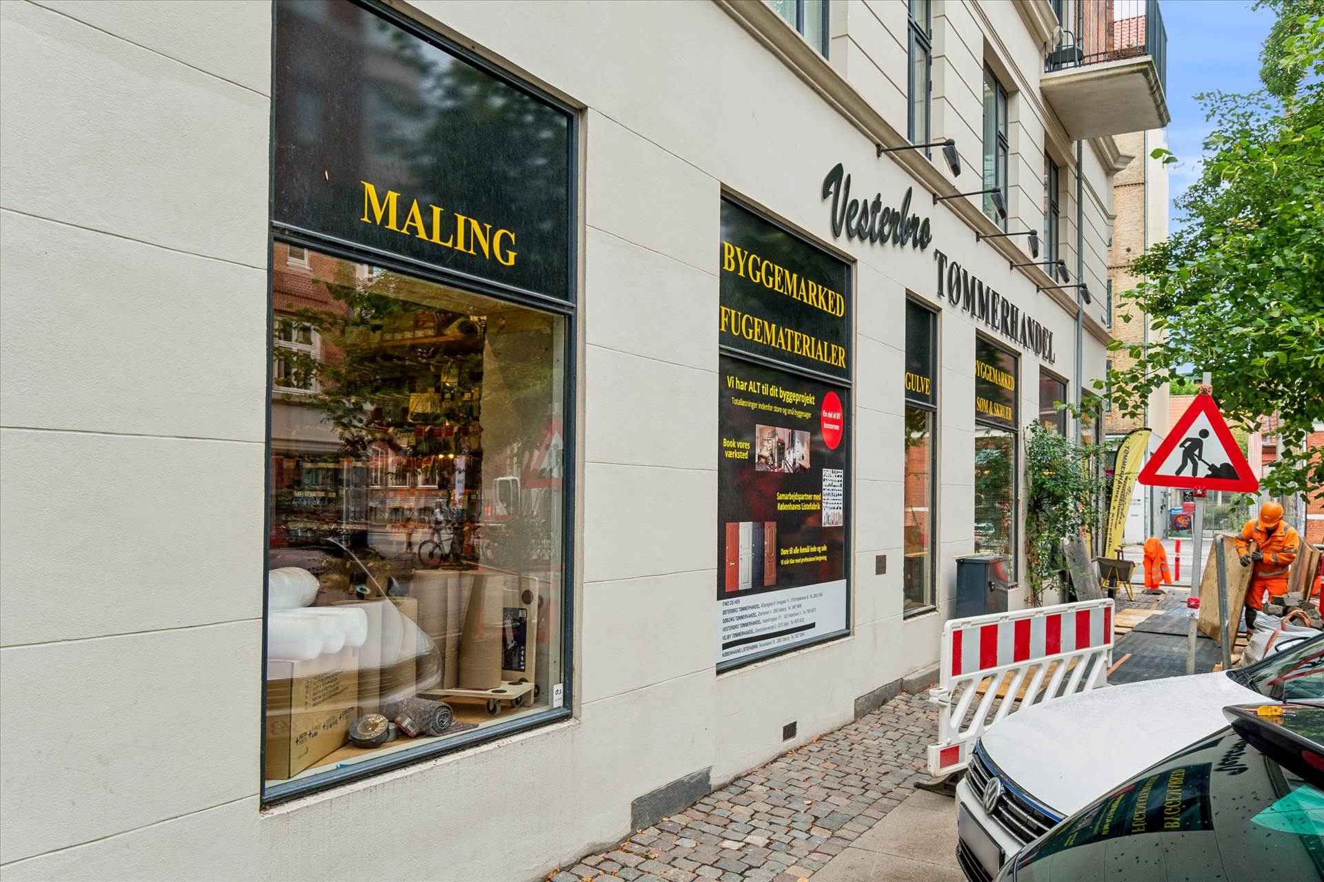 Butiksvindue med udsigt til produkter og reklame. Butiksskilte er oplyst og siger Vesterbro Tometerhandel. En gul-rød