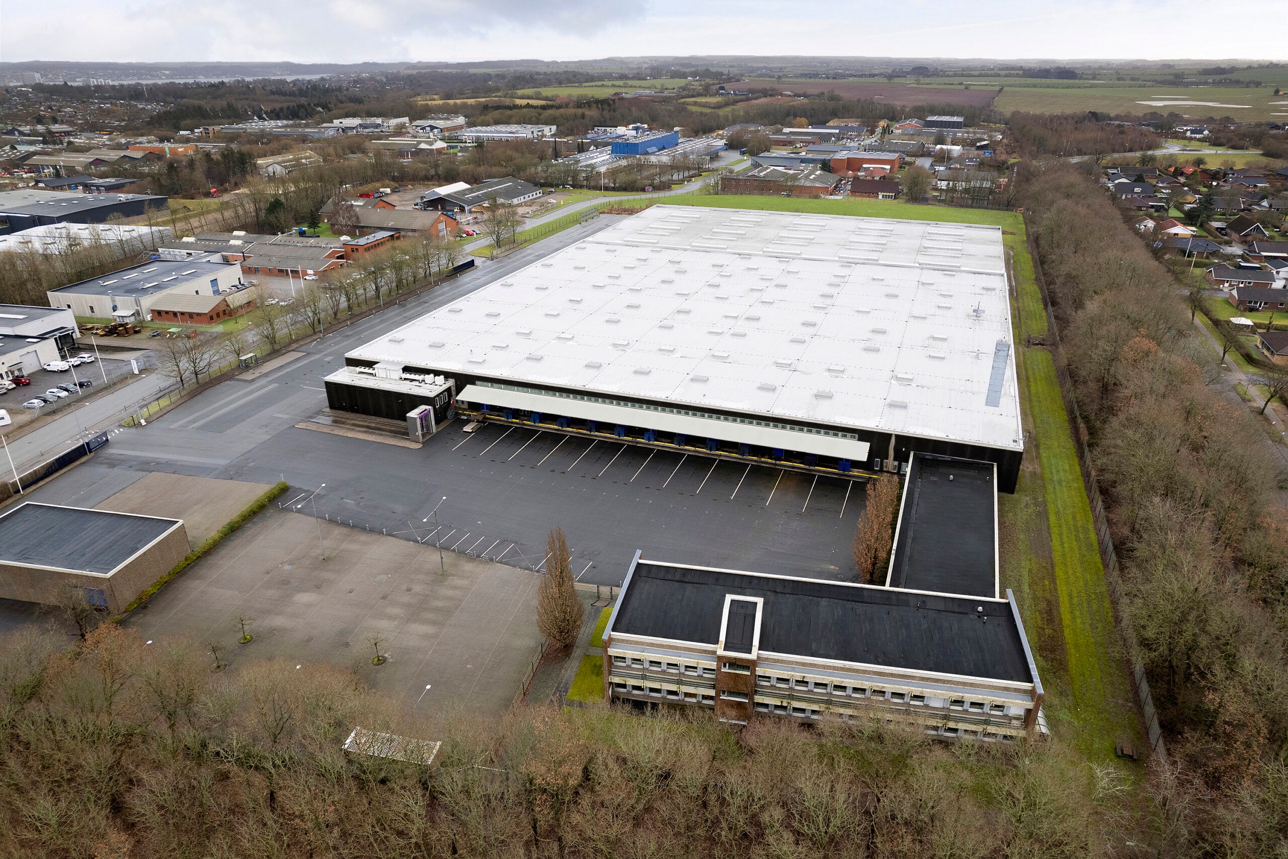 Et stort hvidt lagerbyggeri med store parkeringspladser og en bred grøn græsplæne foran i Kolding