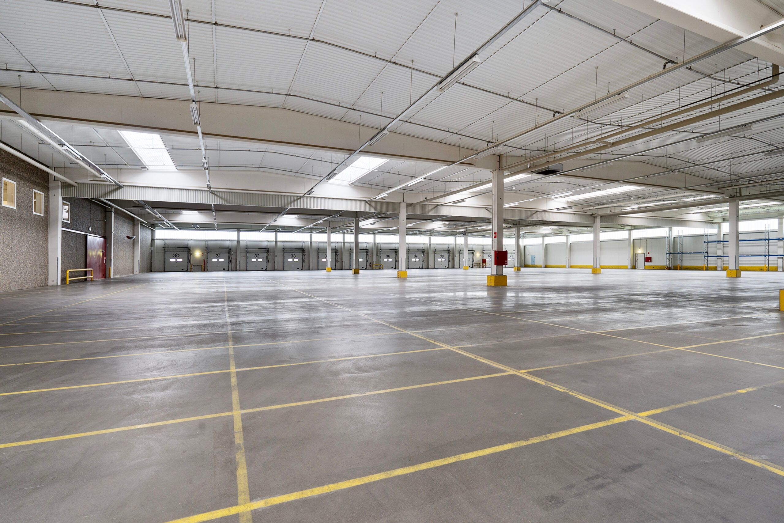 Lagerlokaler i Kolding Syd med moderne lys, store gulvområder og lysegule parkeringslinjer, samt røde døre og højloftede