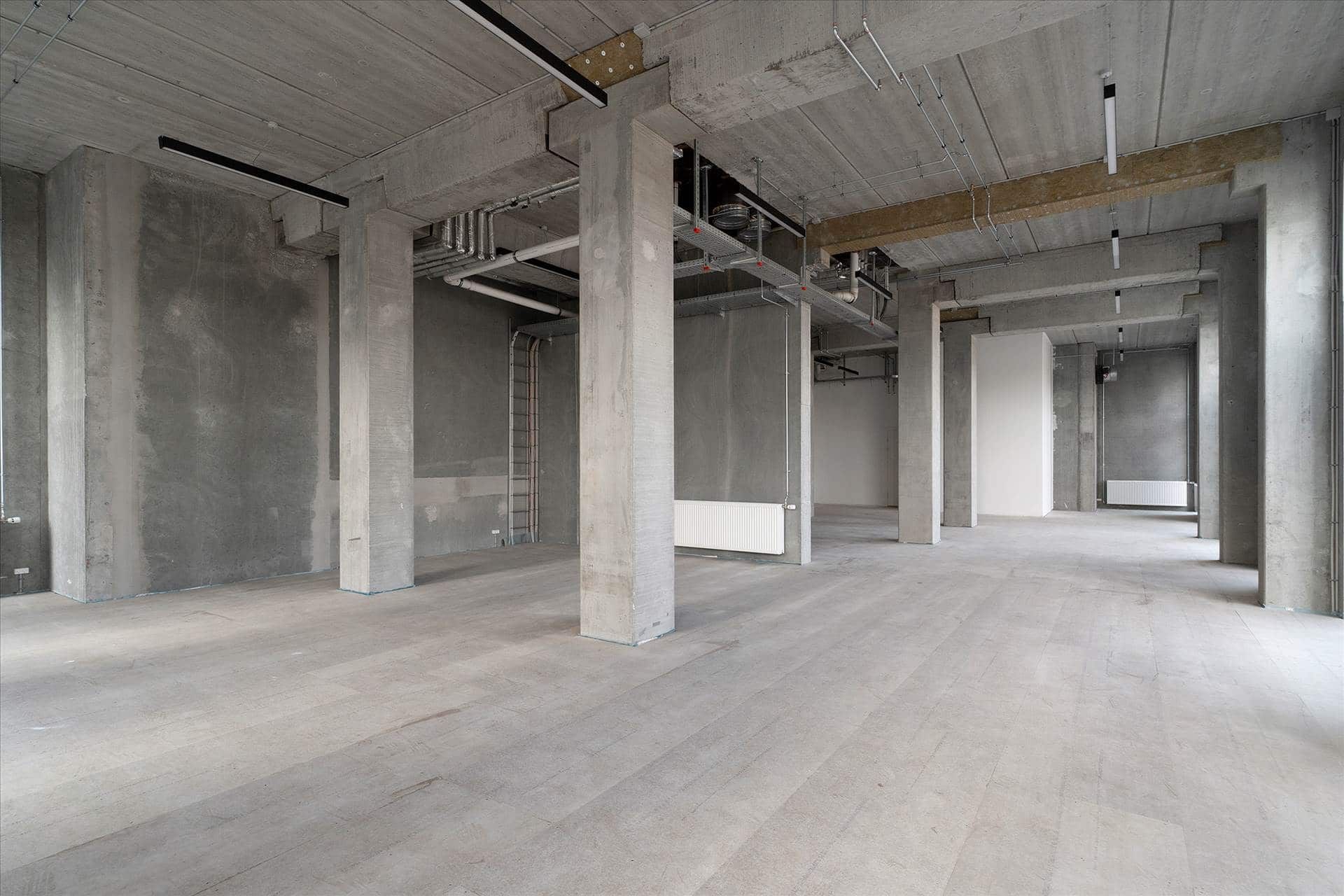 Moderne, industriel industrihal med betongulv, store søjler og åbne lofter med kabelkanaler og ventiler i loftet