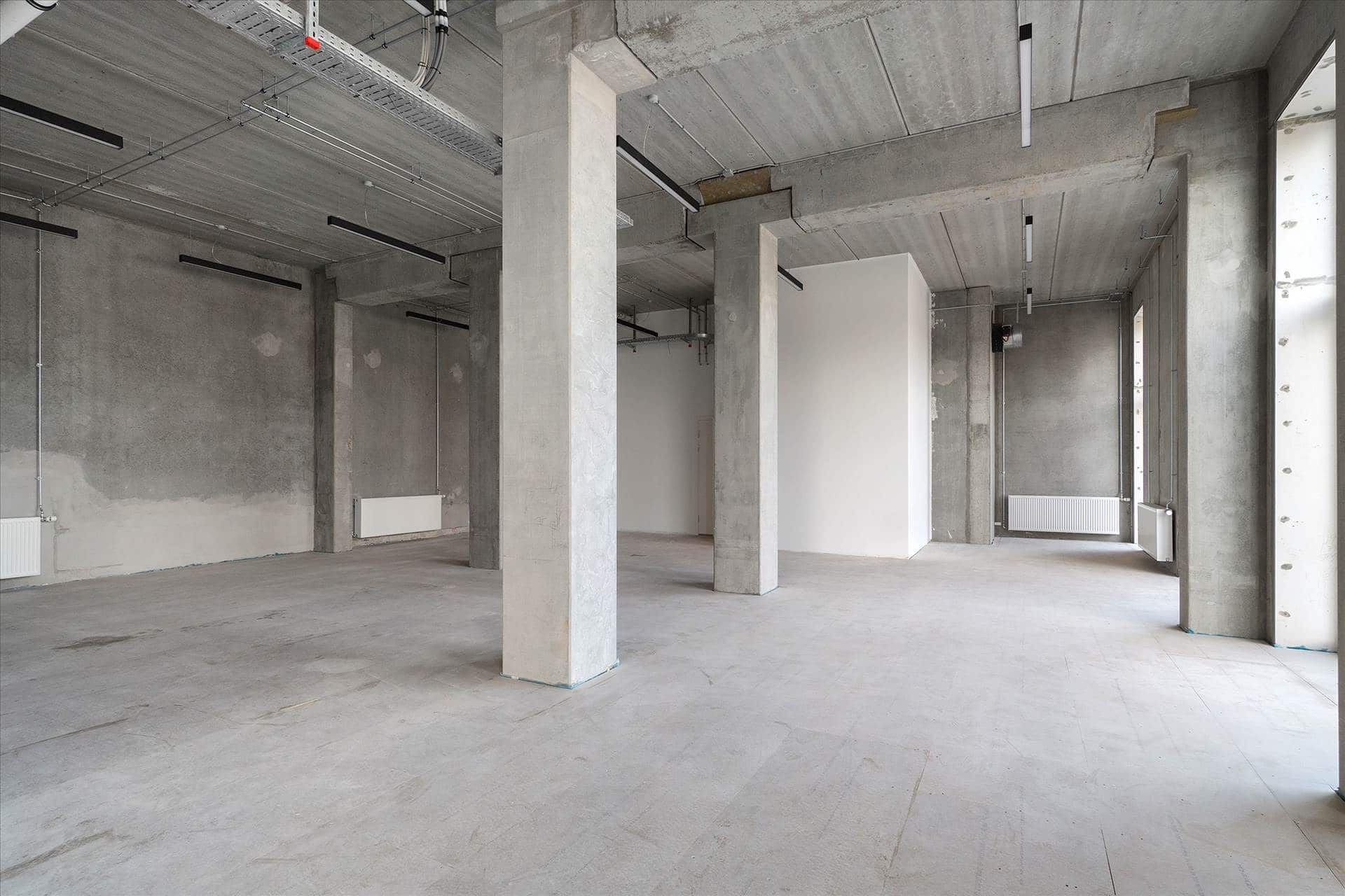 Store erhvervslokaler med højt til loftet og eksponeret beton samt hvide vægge og gulv og store vinduer