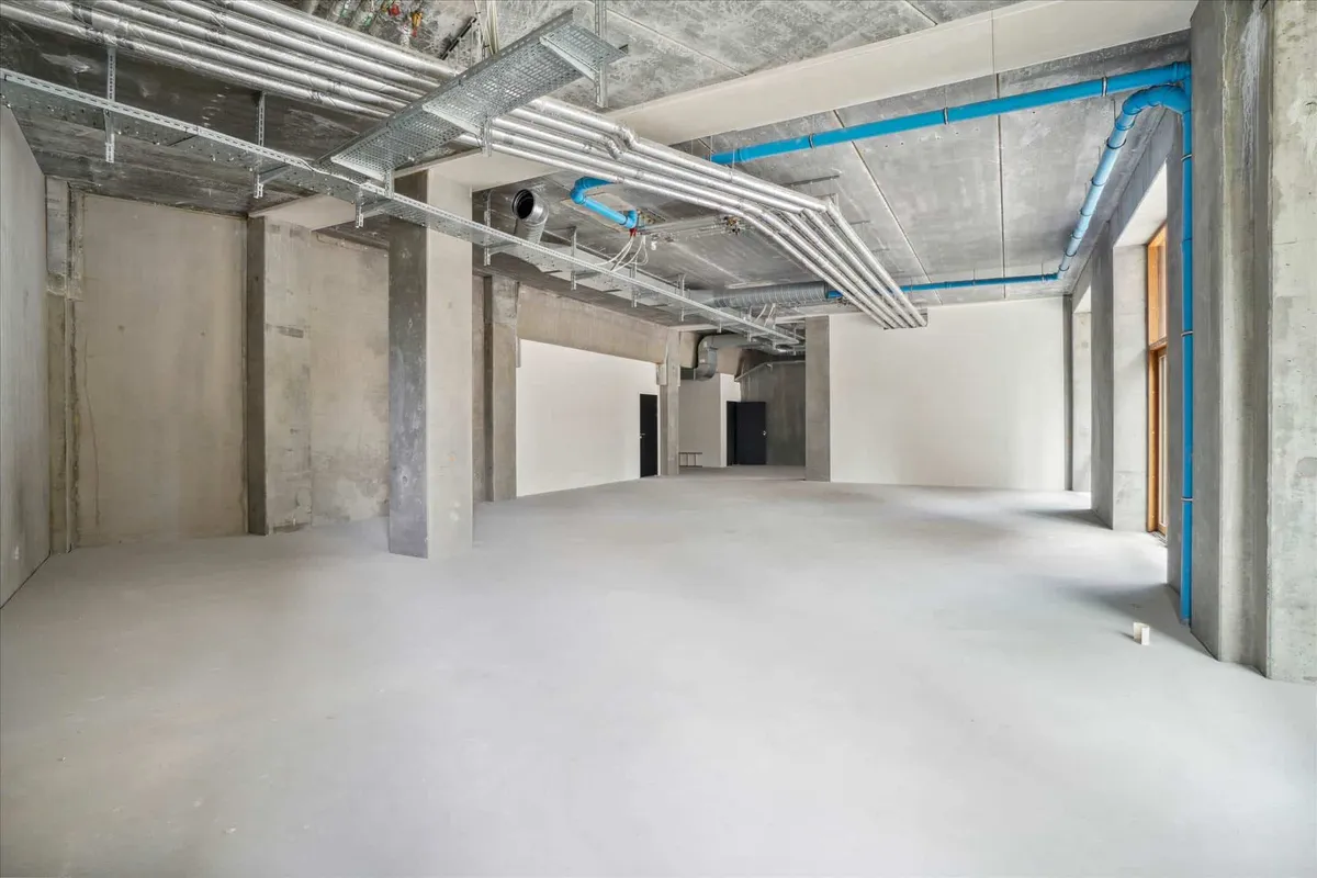 Et stort og højloftet lokale med blanke vægge og gulve samt åbne loftsarealer med synlige rørteknologier