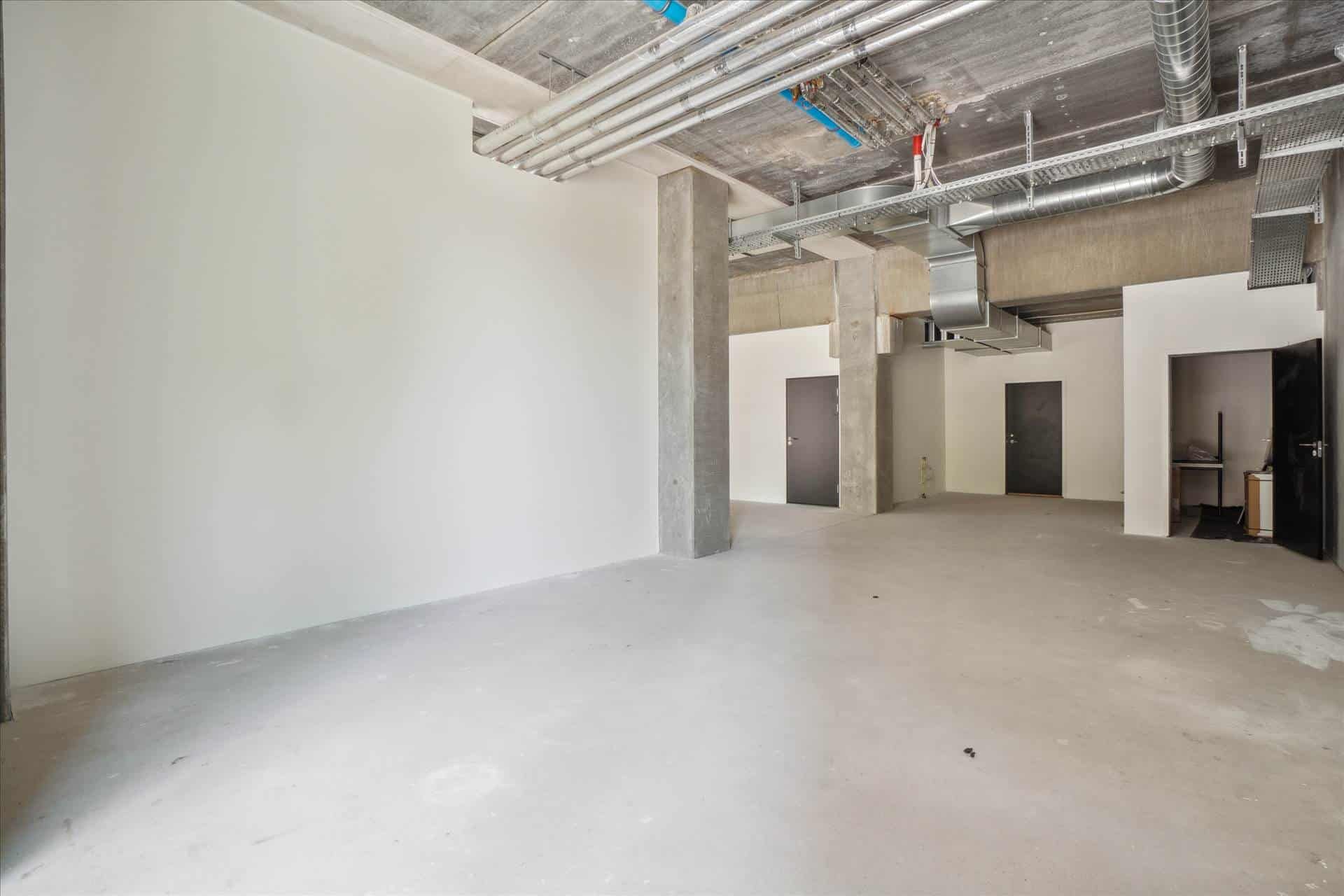 Lejlighed med højloft og to separate værelser og døre. Betongulv og vægge med store vinduer og åbne døre.