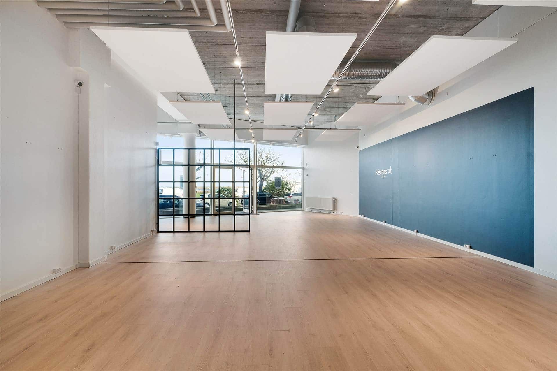 En tom kontorvirksomhed med lyse loftspaneler, gulvbelægning og stående møbler i en afdeling med en stor blå væg med mærke