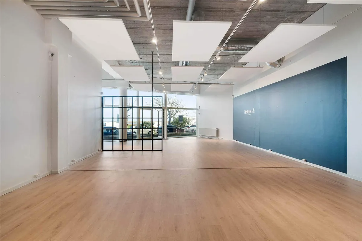 En tom kontorvirksomhed med lyse loftspaneler, gulvbelægning og stående møbler i en afdeling med en stor blå væg med mærke