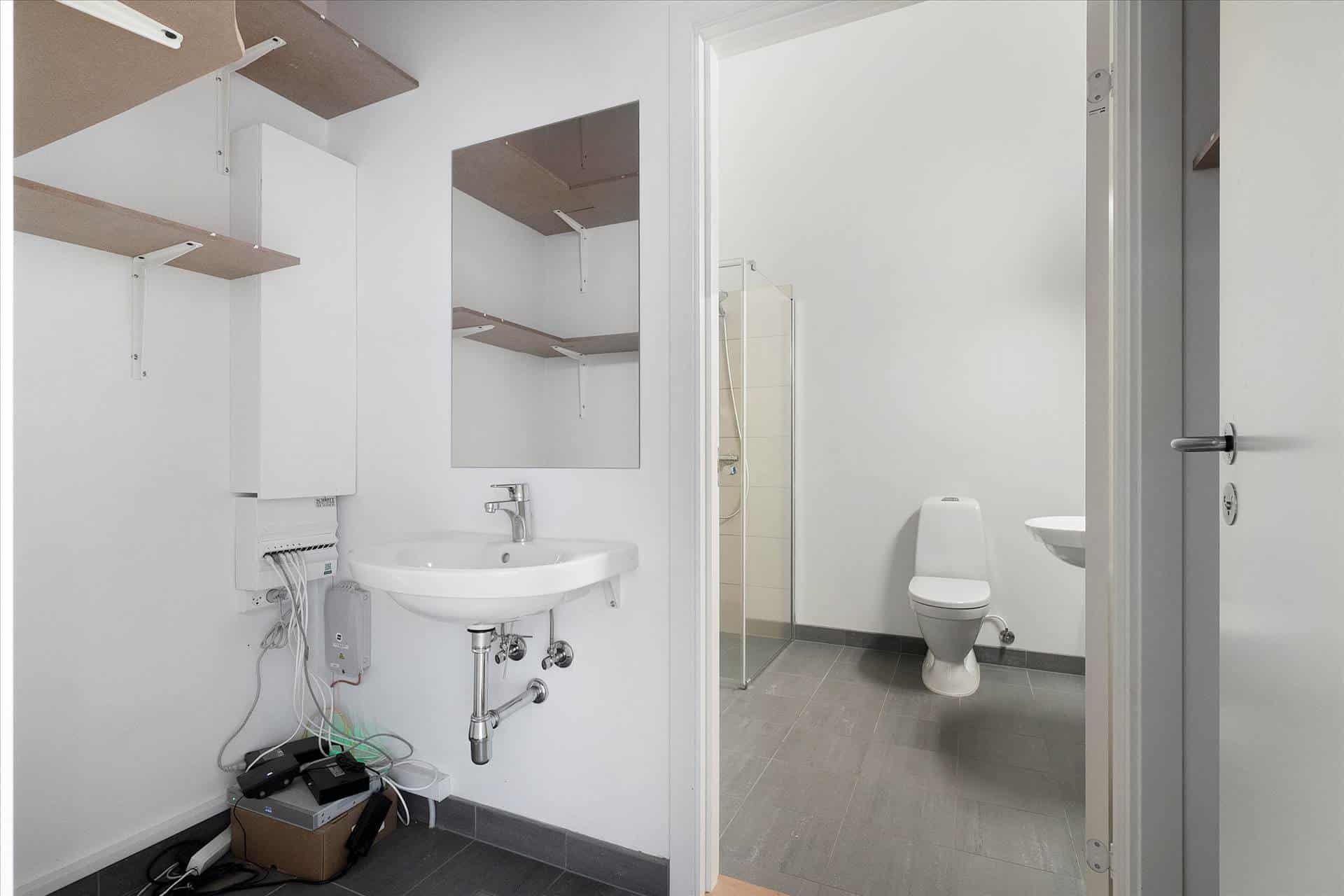 En hvid, moderne badeværelse med højloft og gulv. Toilet og håndvask med spejl og indbyggede hylder.