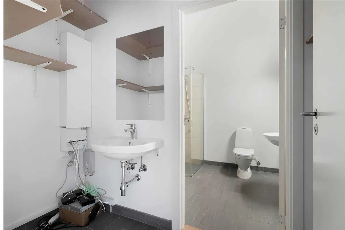 En hvid, moderne badeværelse med højloft og gulv. Toilet og håndvask med spejl og indbyggede hylder.