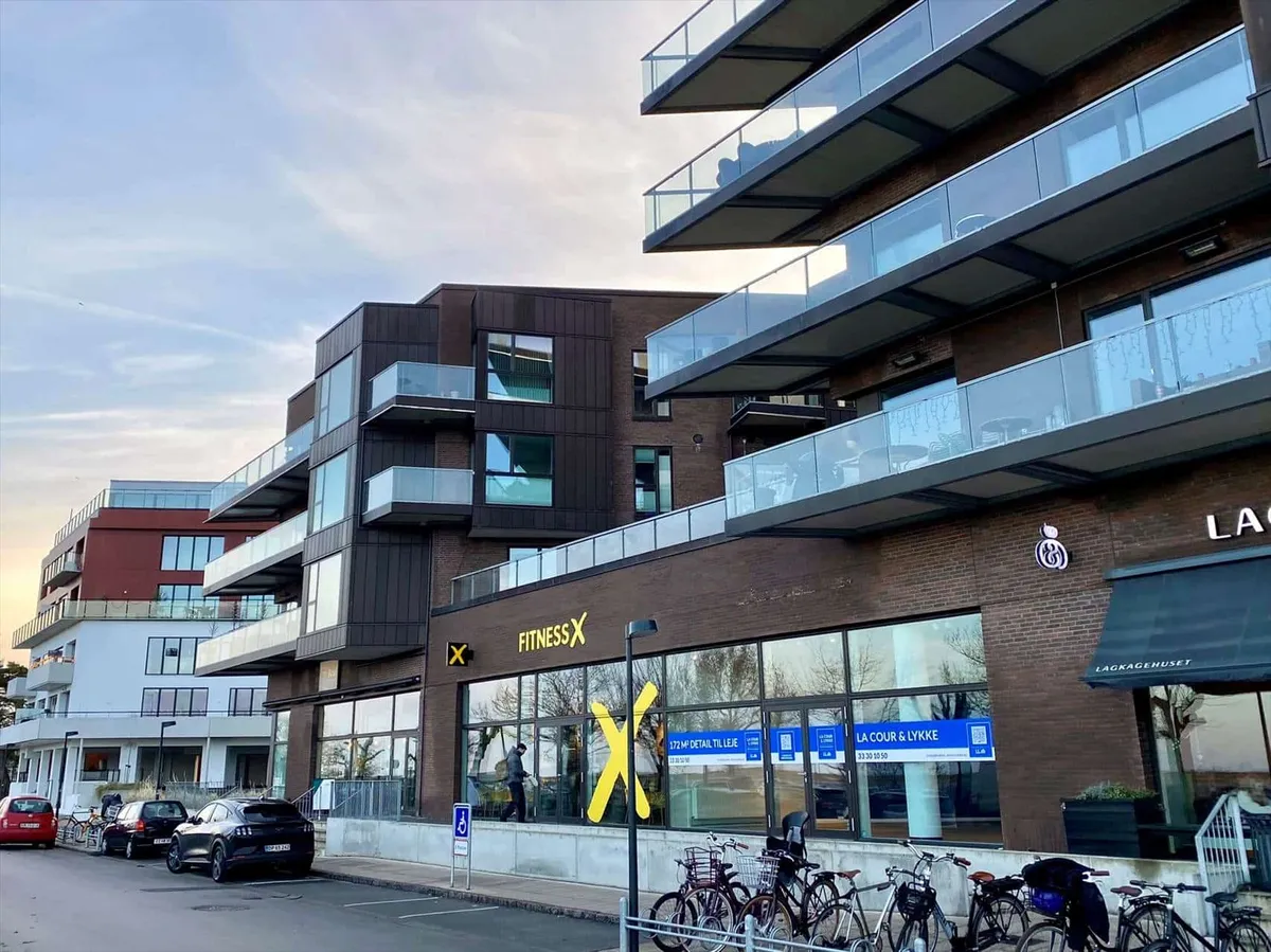 FitnessX butik på Amager Strandvej med store vinduer og lejemålsannonce, hvor en mand går ind