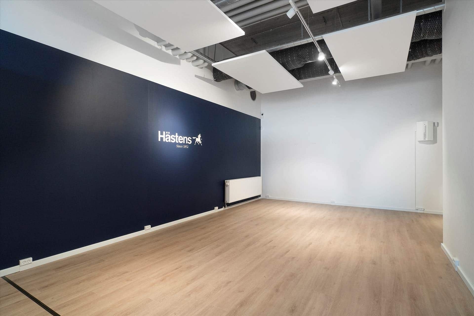 En tom dansk butik med trægulve, hvid og blå væg, hængende lamper og et stort mærke på væggen.