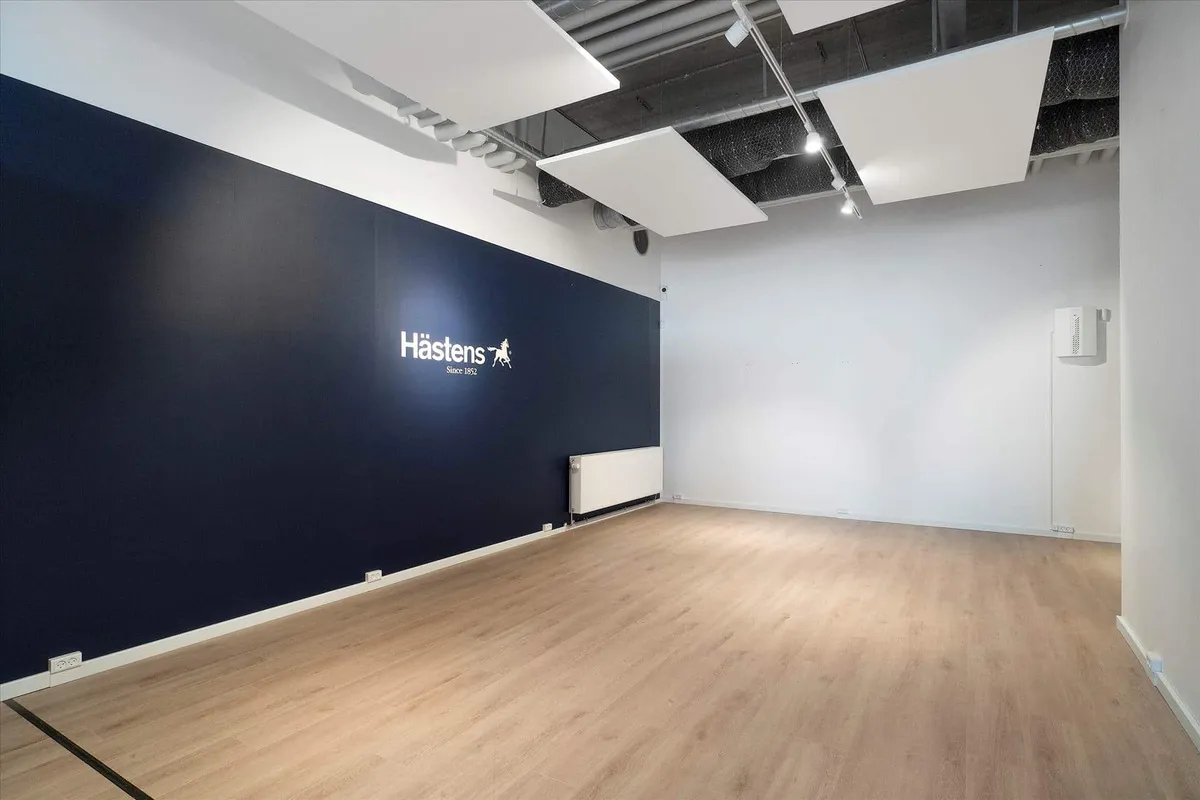 En tom dansk butik med trægulve, hvid og blå væg, hængende lamper og et stort mærke på væggen.