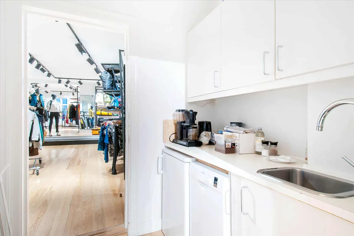 Et hvidt køkken med en skabrække, en vandhane og en vaskemaskine. Der er en kaffemaskine og en tallerken med et håndklæde på