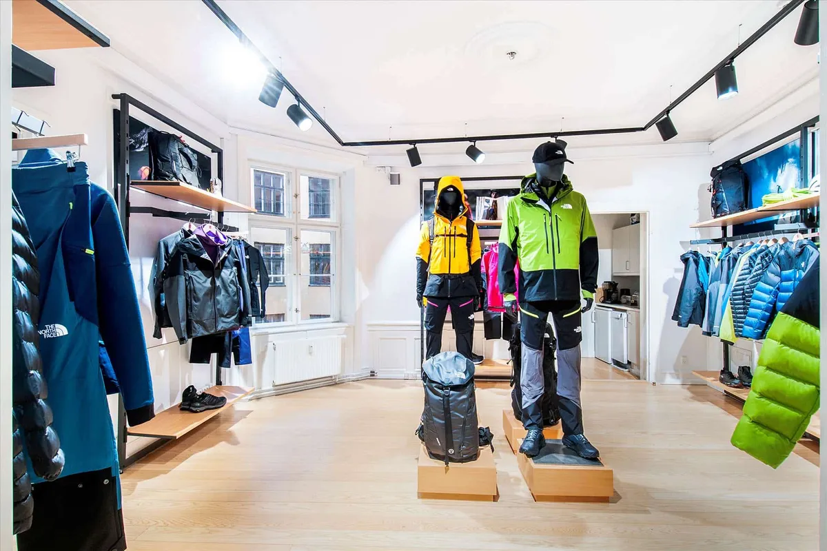 En butik med North Face-tøj og udstyr, med mandsdummies iført sportsjakker og bukser, samt en rygsæk i midten og vinduer med