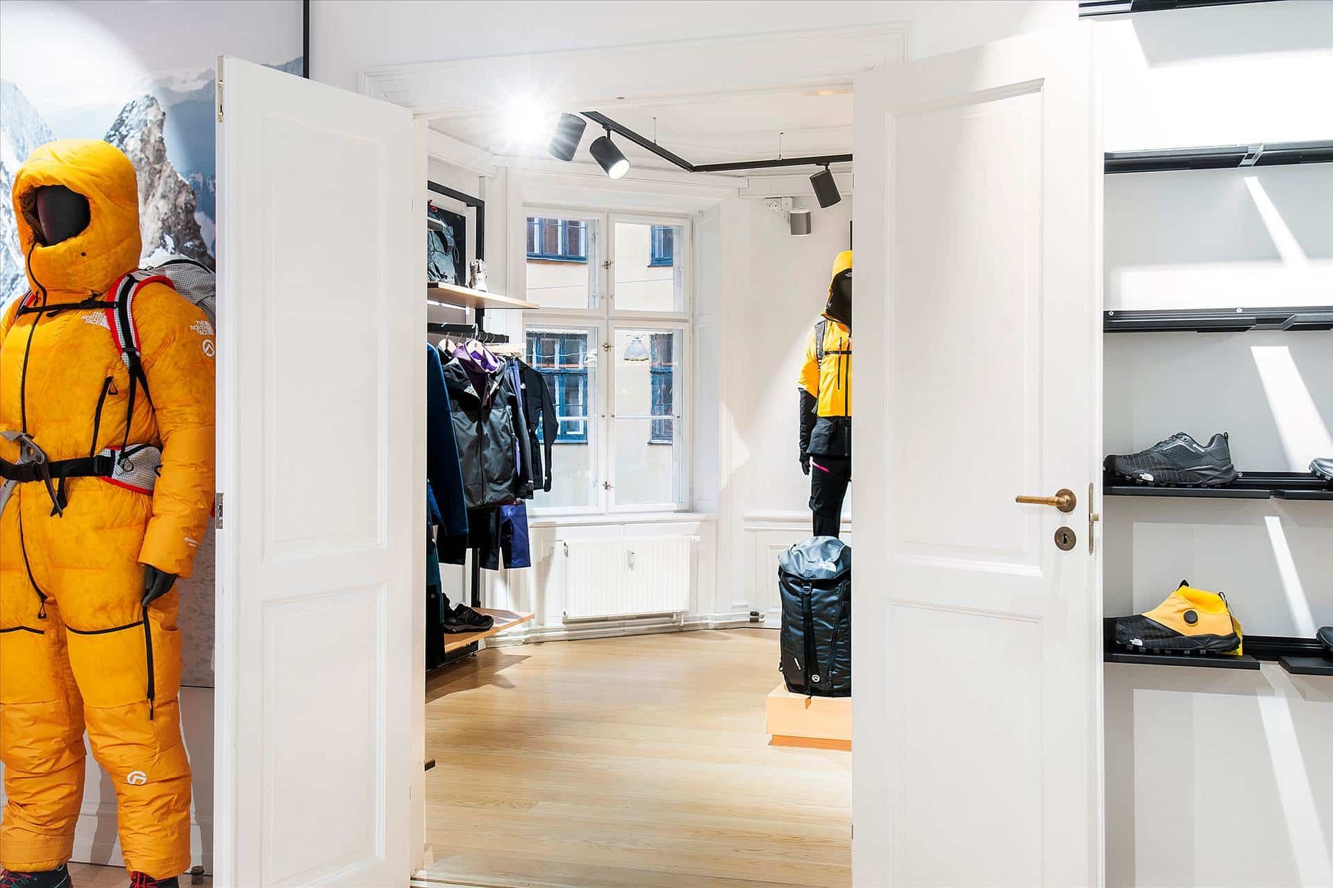 Butik med hvide døre, der vender mod hinanden, og udskåret North Face tøj og udstyr i det. Gule North Face-kostumer og