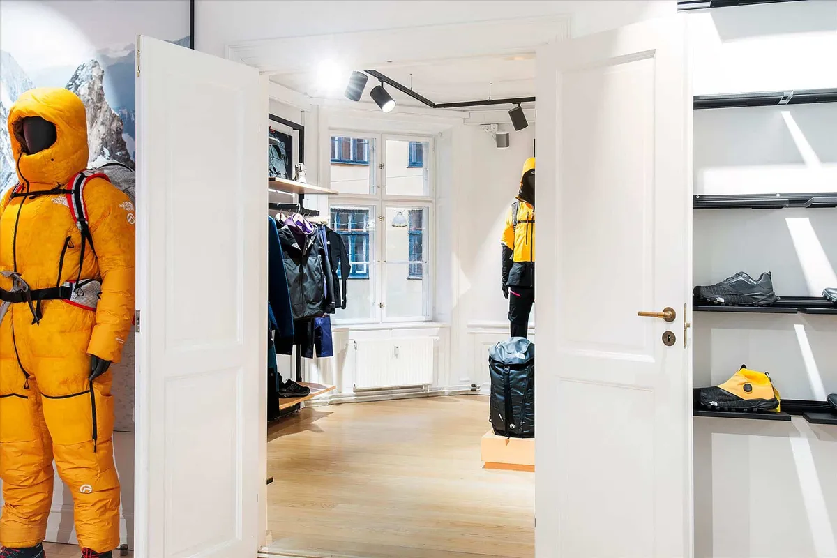 Butik med hvide døre, der vender mod hinanden, og udskåret North Face tøj og udstyr i det. Gule North Face-kostumer og