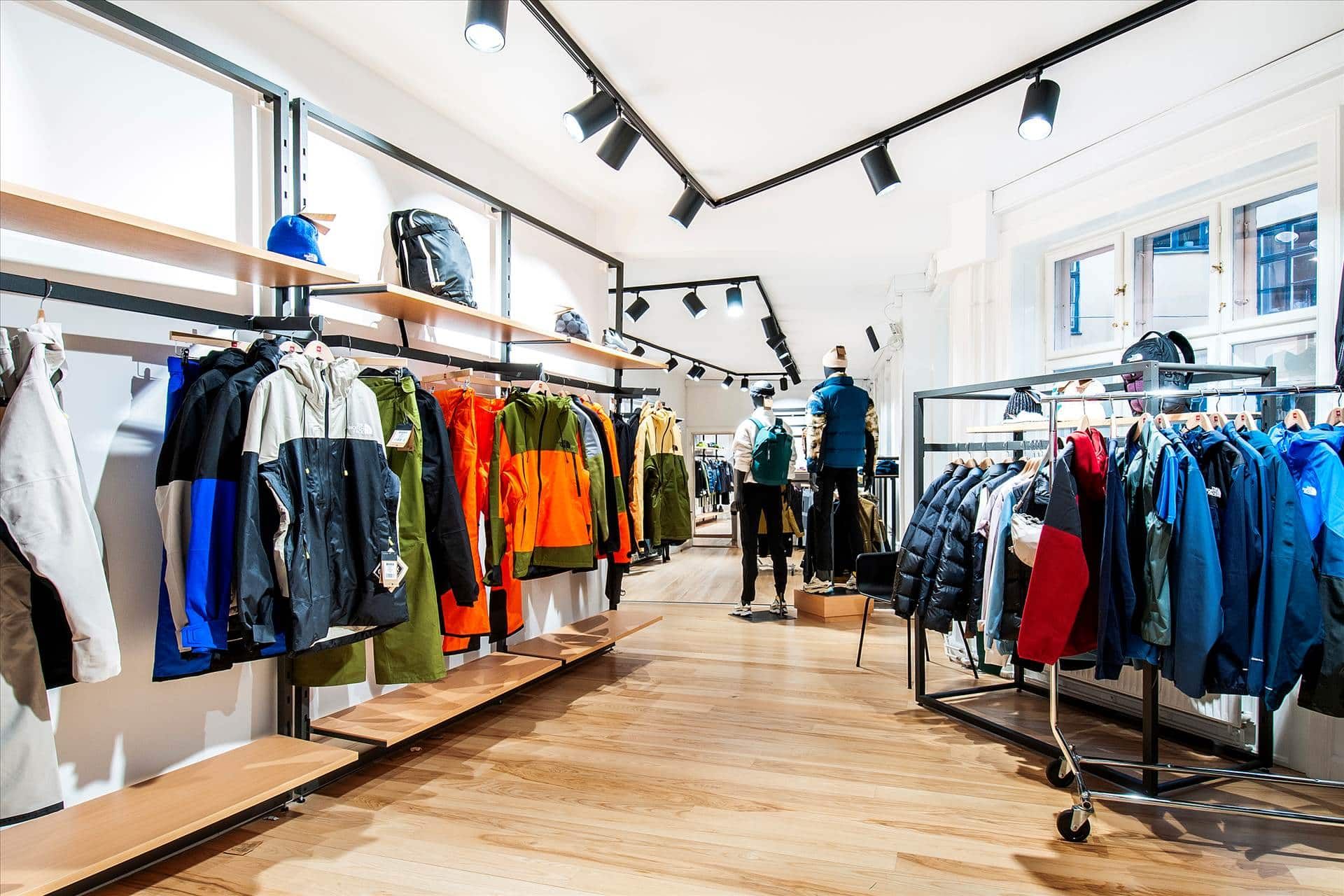 Klædeskab med hængende jakkesæt og sko. Der er skrift på en af jakkerne. To figurstative med tøj og en mand med rygsæk og