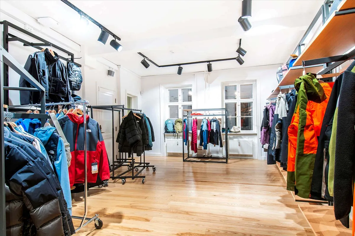 Store med tøj og jakkestativer i store mængder med lyse og mørke farver. Alle tøj er hængt op og der er flere tøjstativer i