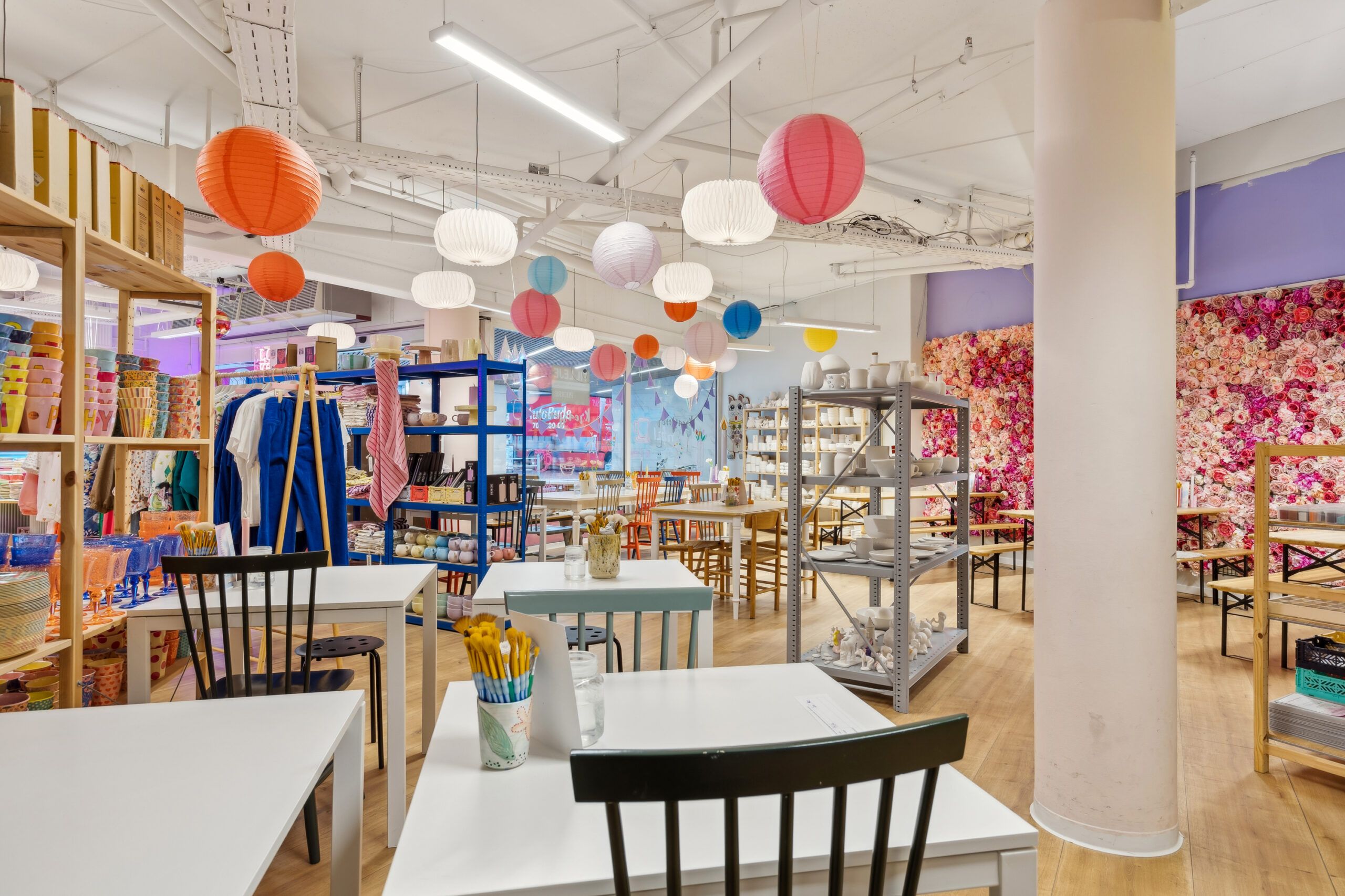 Køkkenborde med tallerkener og krus samt søjler i en forretning med farverige papirlakker i loftet