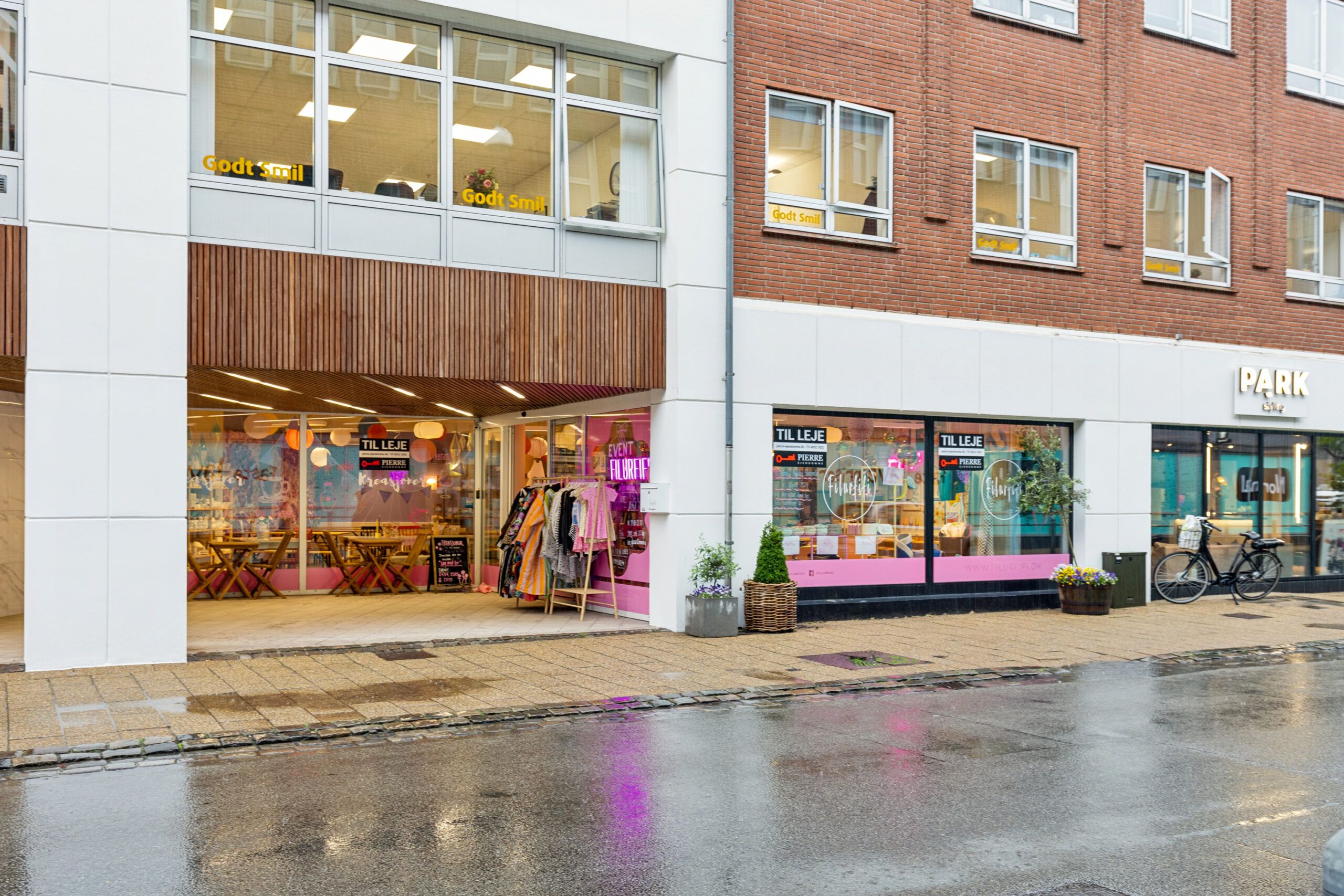 Københavnsgade er en gågade med flere butikker og caféer, træerne og planterne, og en cykel parkeret på fortovet.