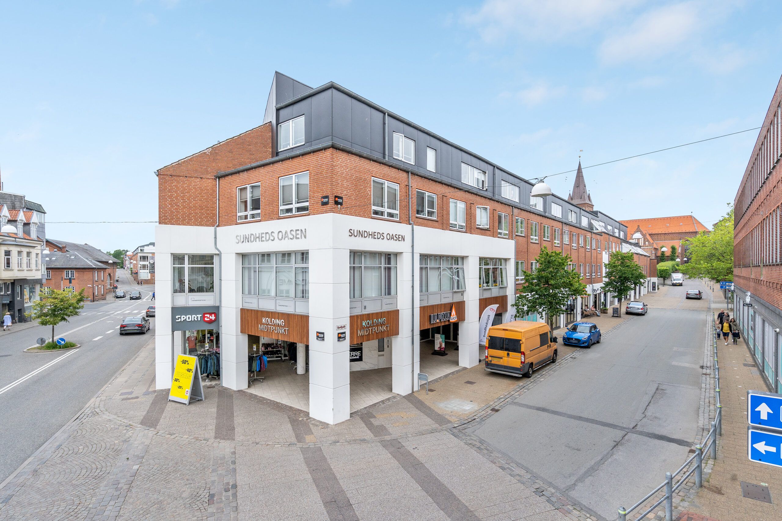 Hjørnelejemål i Kolding bymidte med store vinduer og facader i røde mursten og hvide paneler