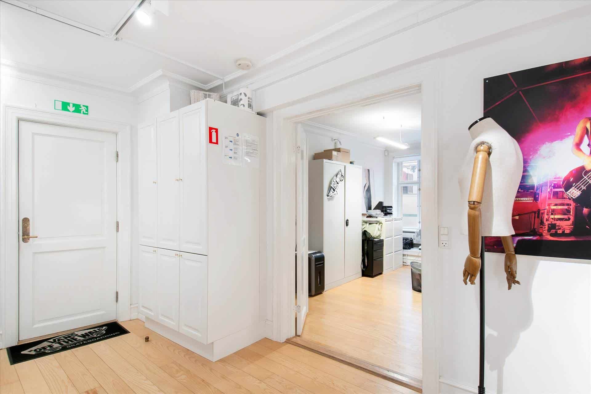 Køkken med vandkøleskab, trægulv og åbent kammer, ligesom der er en manuel ståstol og et foto af en musiker på væggen